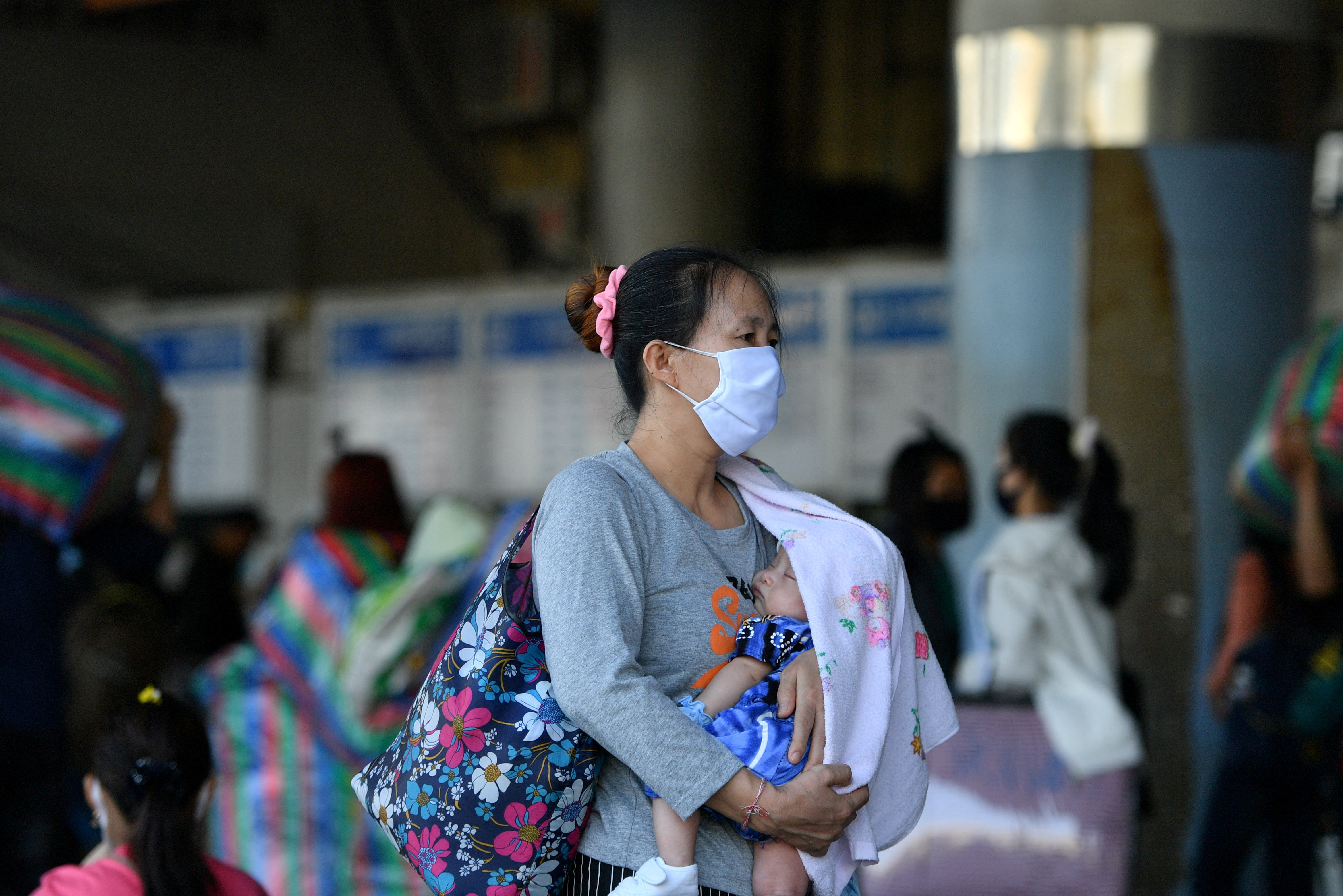 A woman wearing a mask carries a baby at a bus station during the coronavirus disease (COVID-19) outbreak, in Bangkok