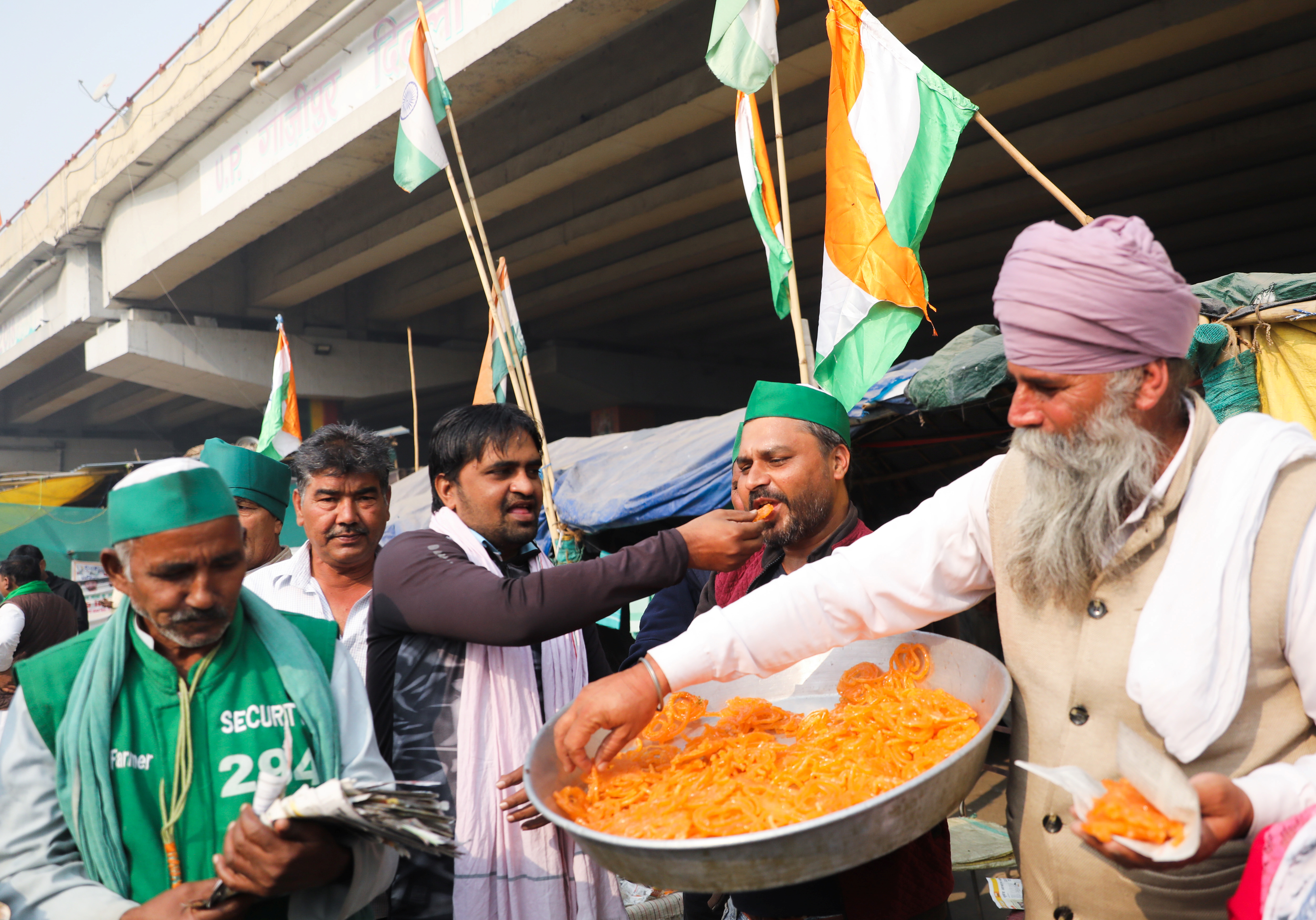 Farmers feed each other sweets and celebrate as they pose for pictures after Indian Prime Minister Narendra Modi announced that he will repeal the controversial farm laws, at the Ghazipur farmers protest site near Delhi-UP border