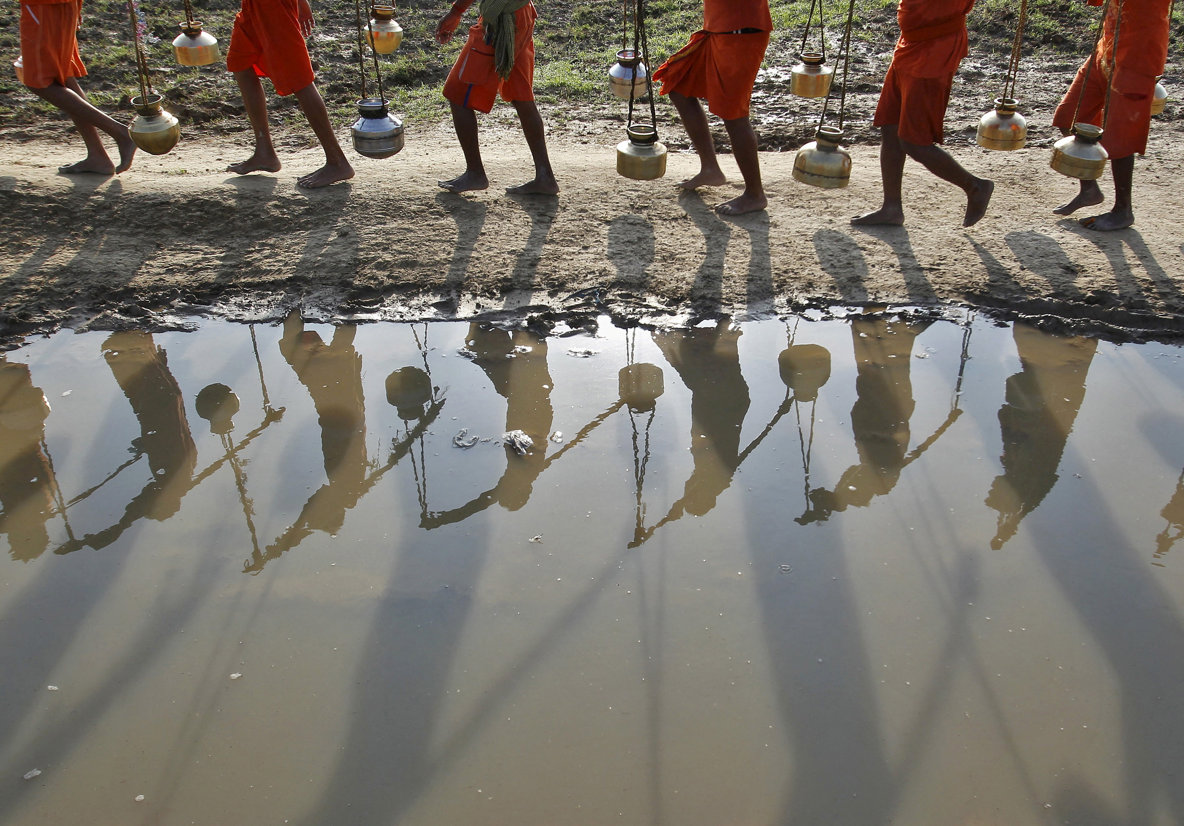 Kanwarias or devotees of Hindu god Shiva carrying pitchers are reflected in a puddle as they walk after filling the pitchers with water from the river Ganges in Allahabad