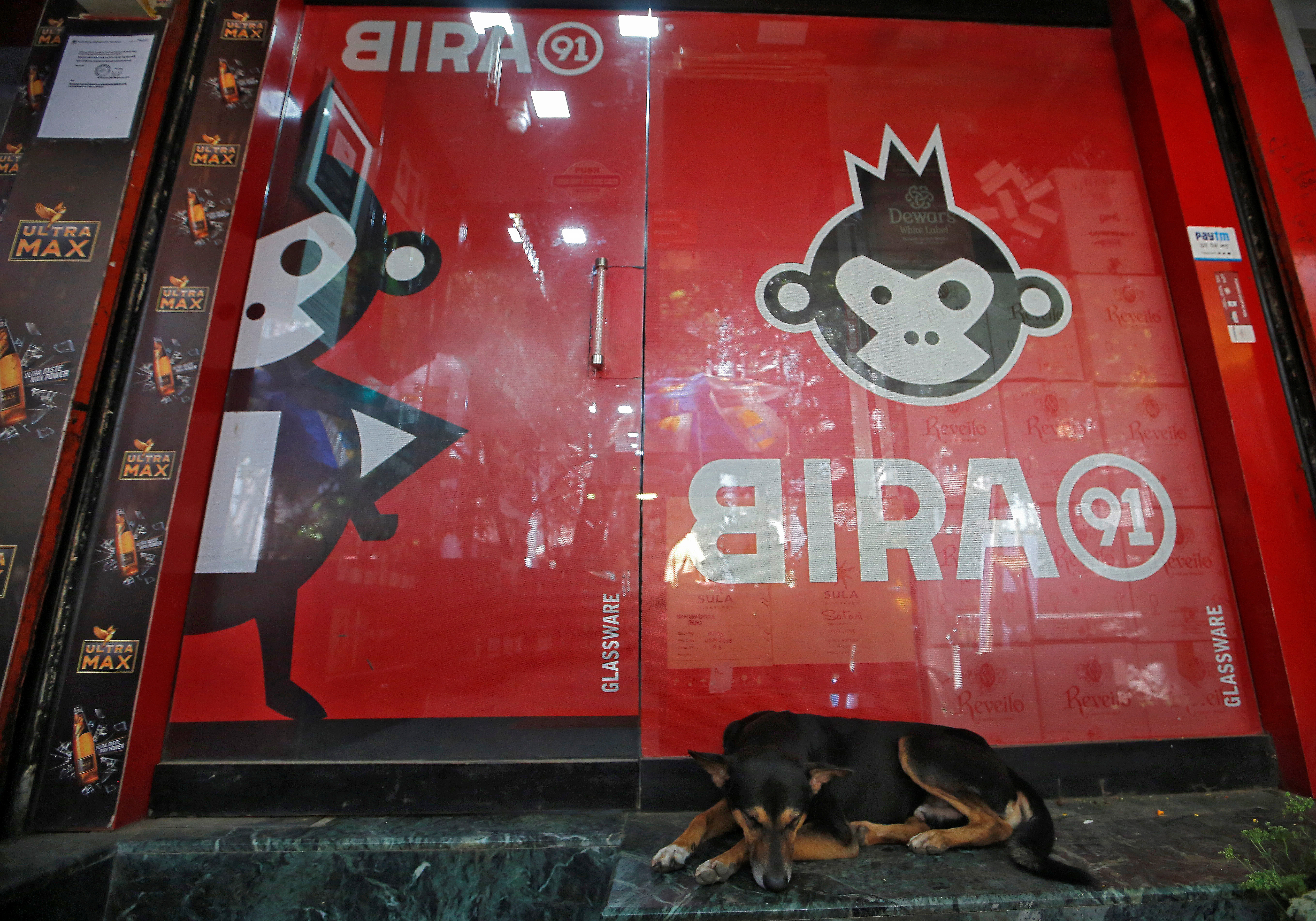 A stray dog rests outside a liquor store with a Bira beer advertisement on it in Mumbai