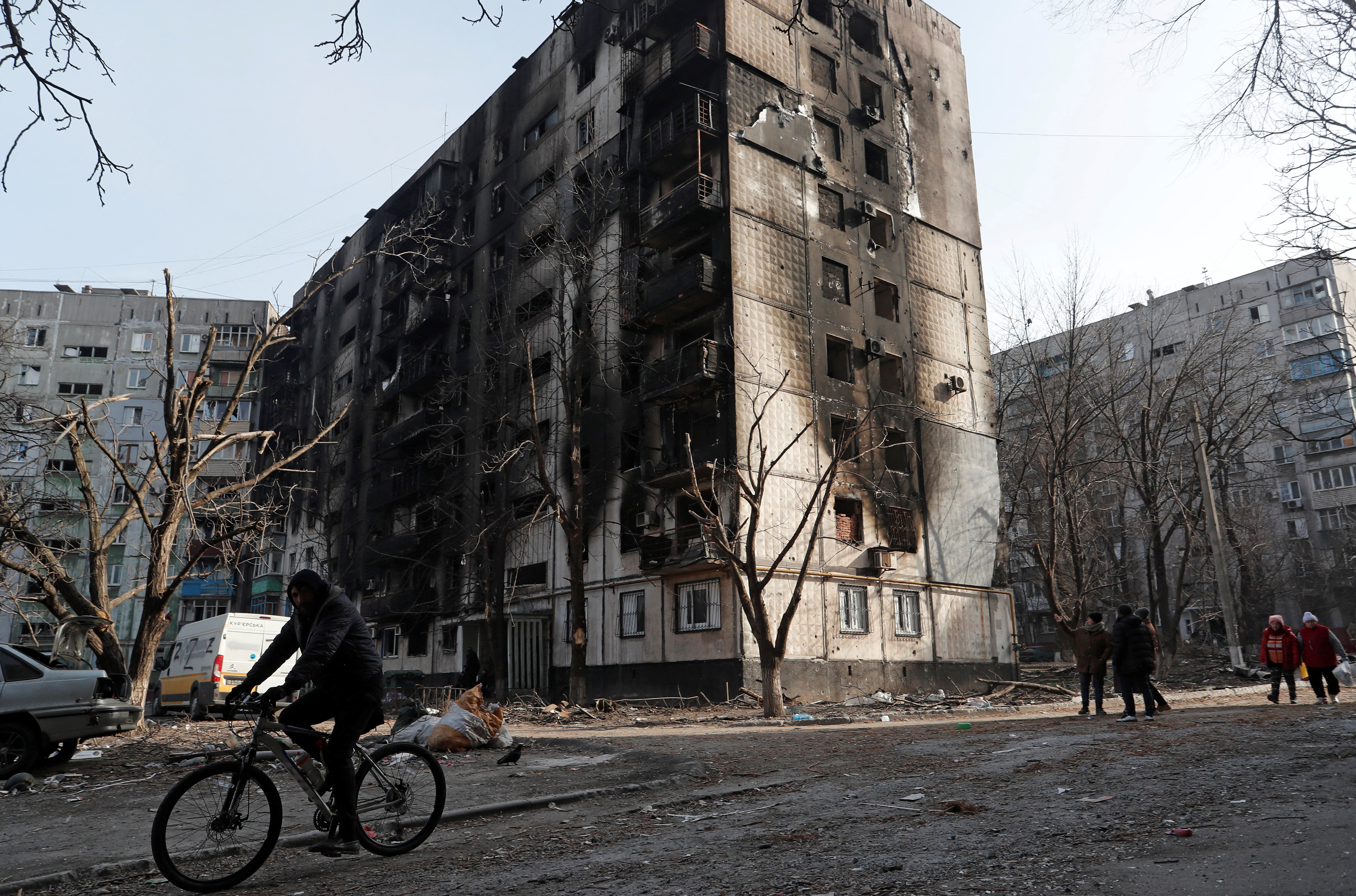 A local resident rides a bicycle past a damaged apartment building in Mariupol