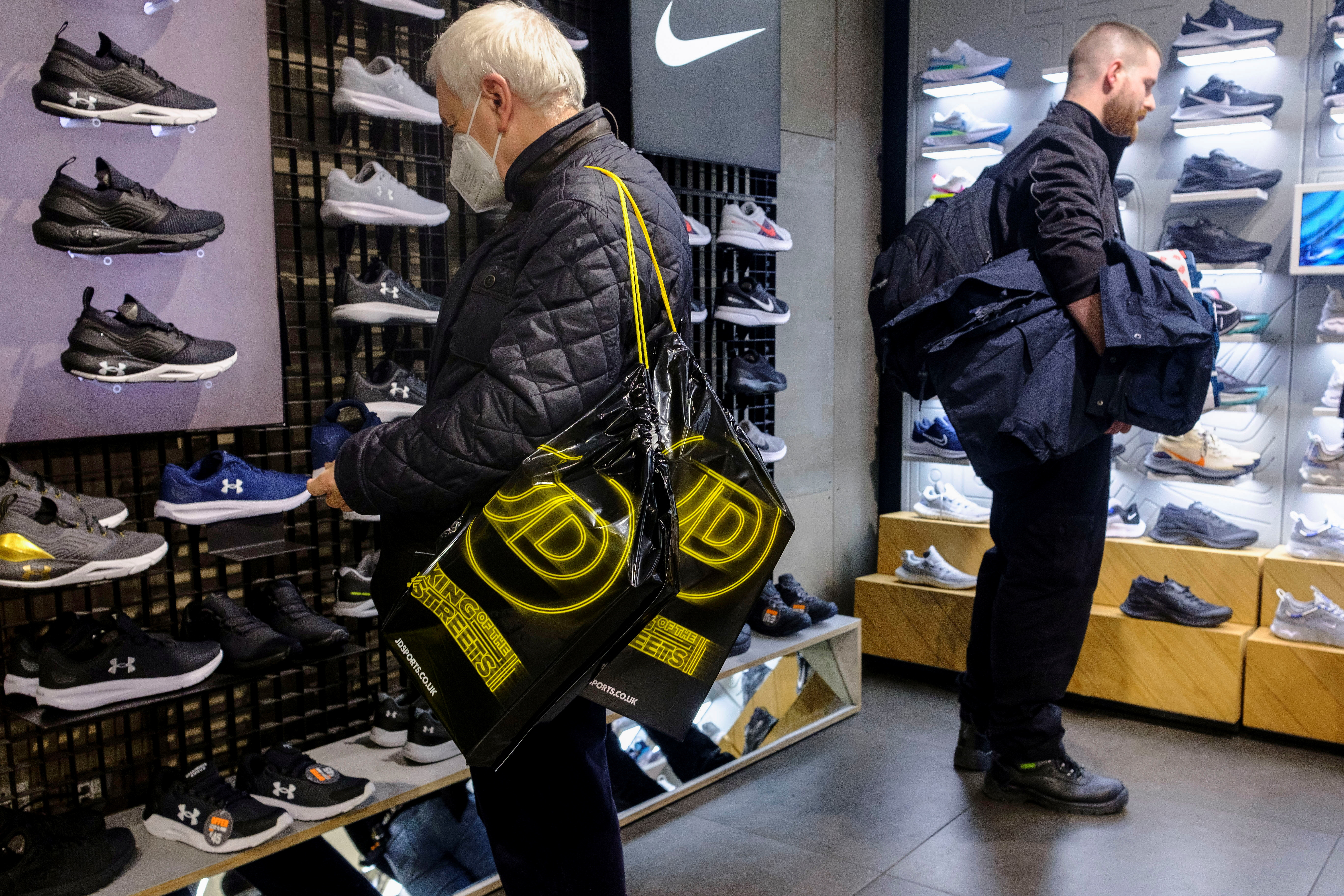A shopper carrying JD Sports bags looks at footwear at a JD Sports store in London