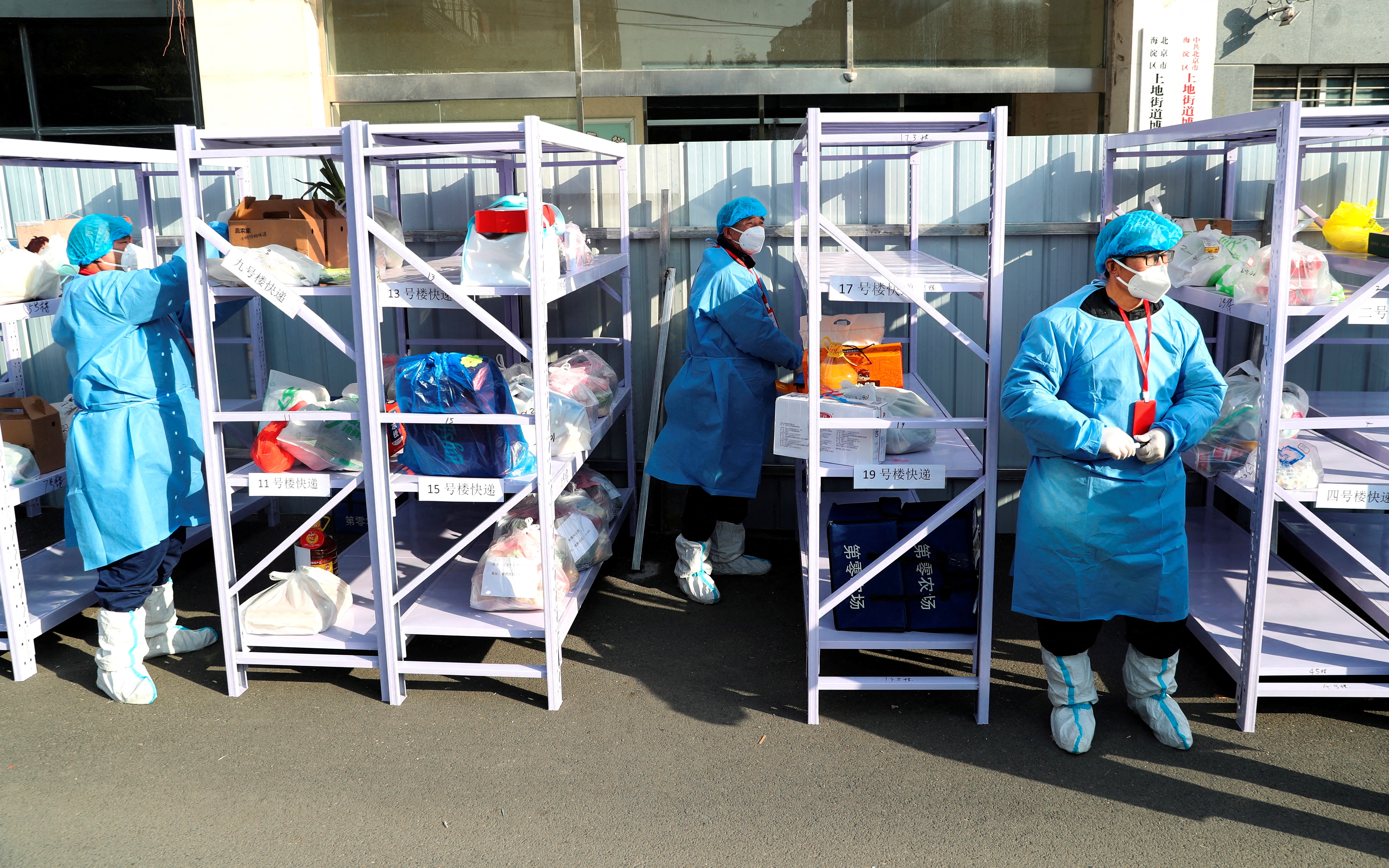 Workers wearing protective suits following the coronavirus disease (COVID-19) outbreak stand next to daily necessities placed on makeshift delivery racks, at a residential compound under lockdown after a case of the Omicron variant was detected, in Beijing's Haidian district, China January 18, 2022. China Daily via REUTERS