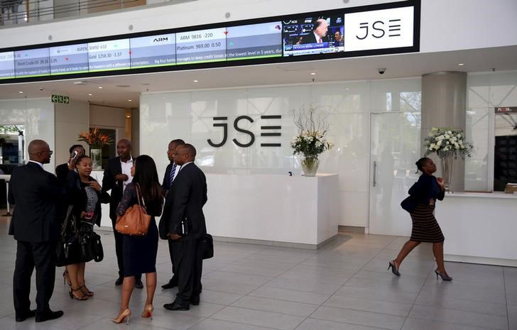 People chat in front of a reception with an electronic board displaying movements in major indices at the Johannesburg Stock Exchange building in Sandton Johannesburg