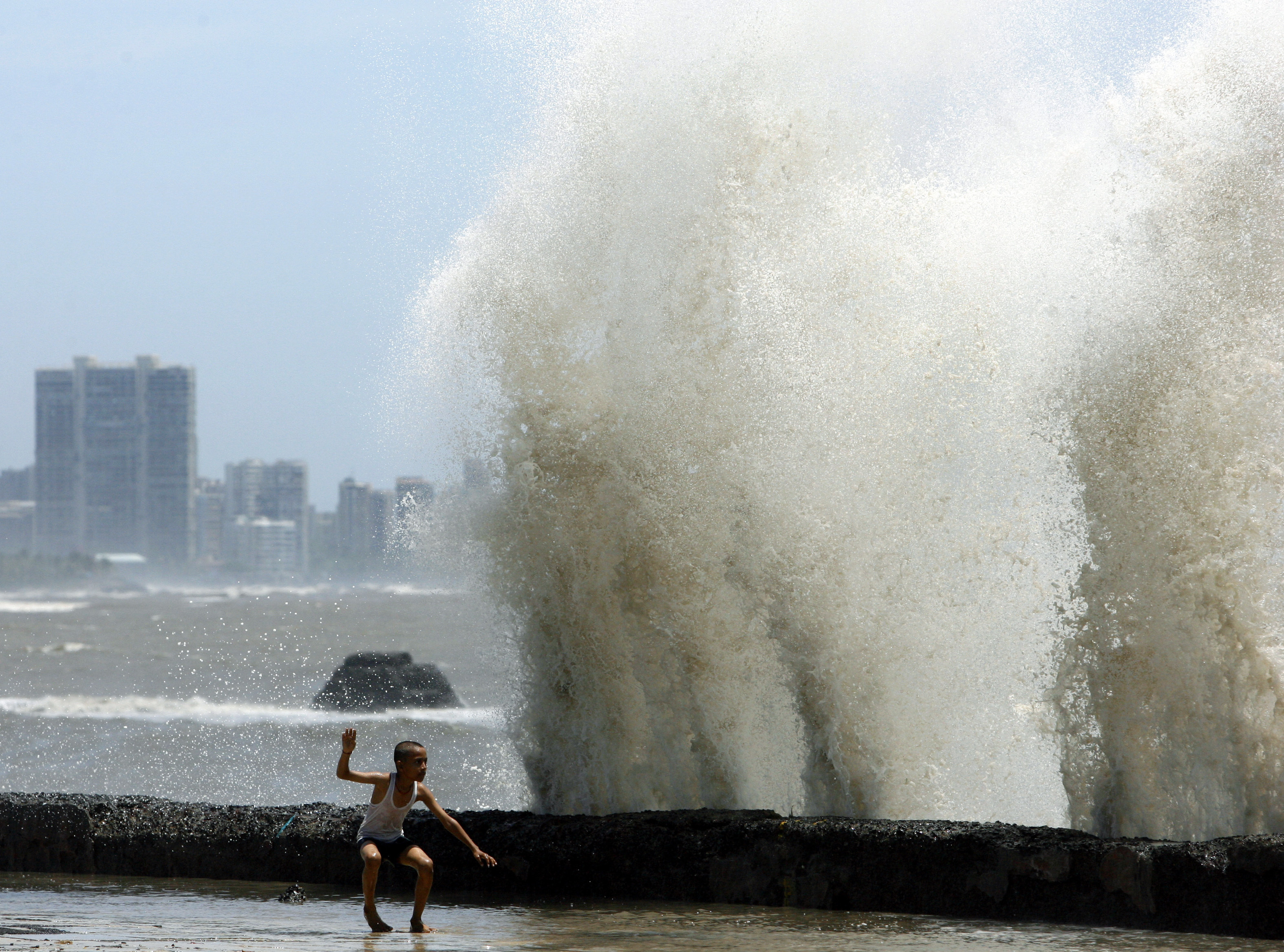 A boy plays under large waves from the Arabian sea crashing against a seawall in Mumbai