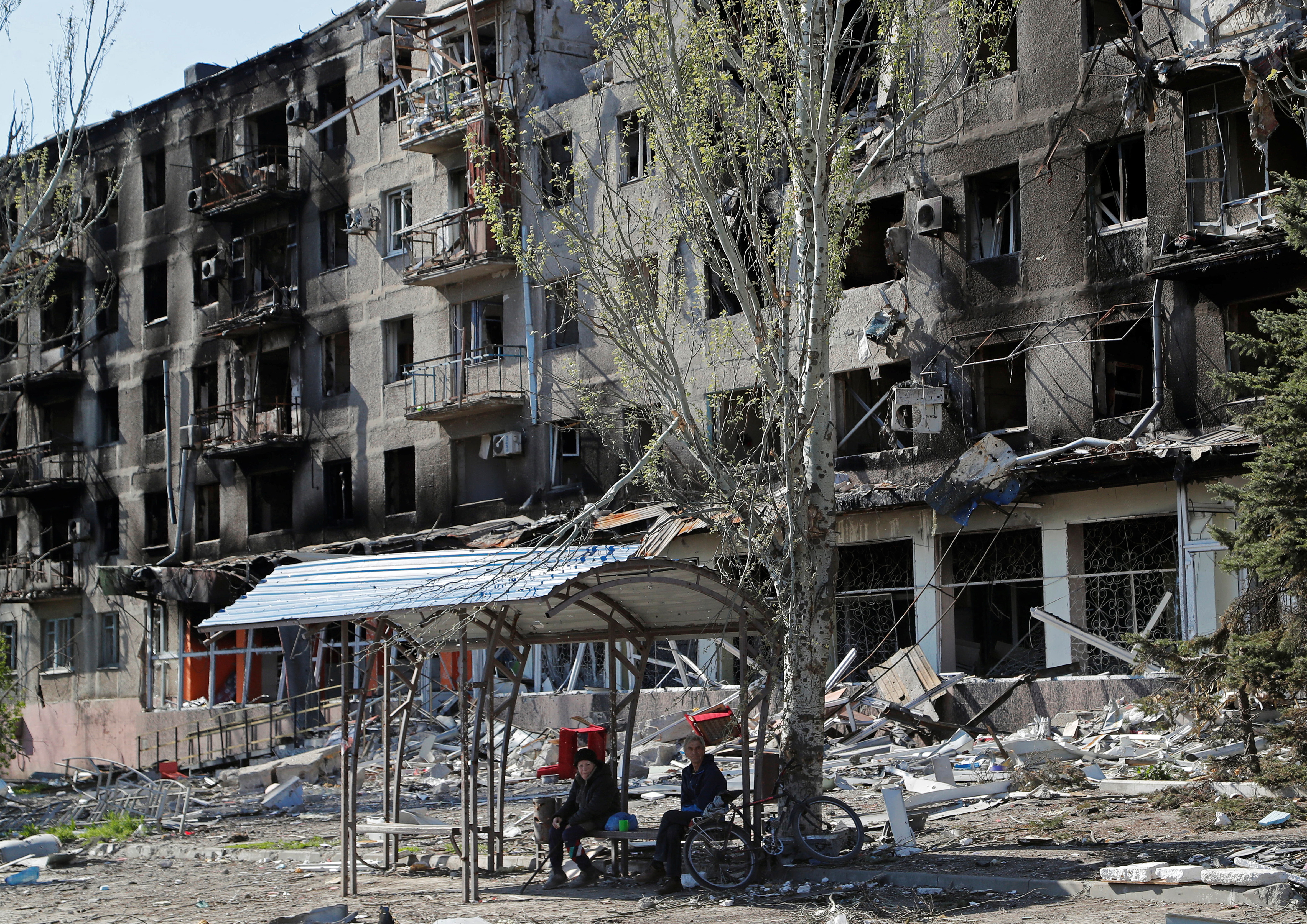 Local residents sit on a bench near a damaged apartment building in Mariupol