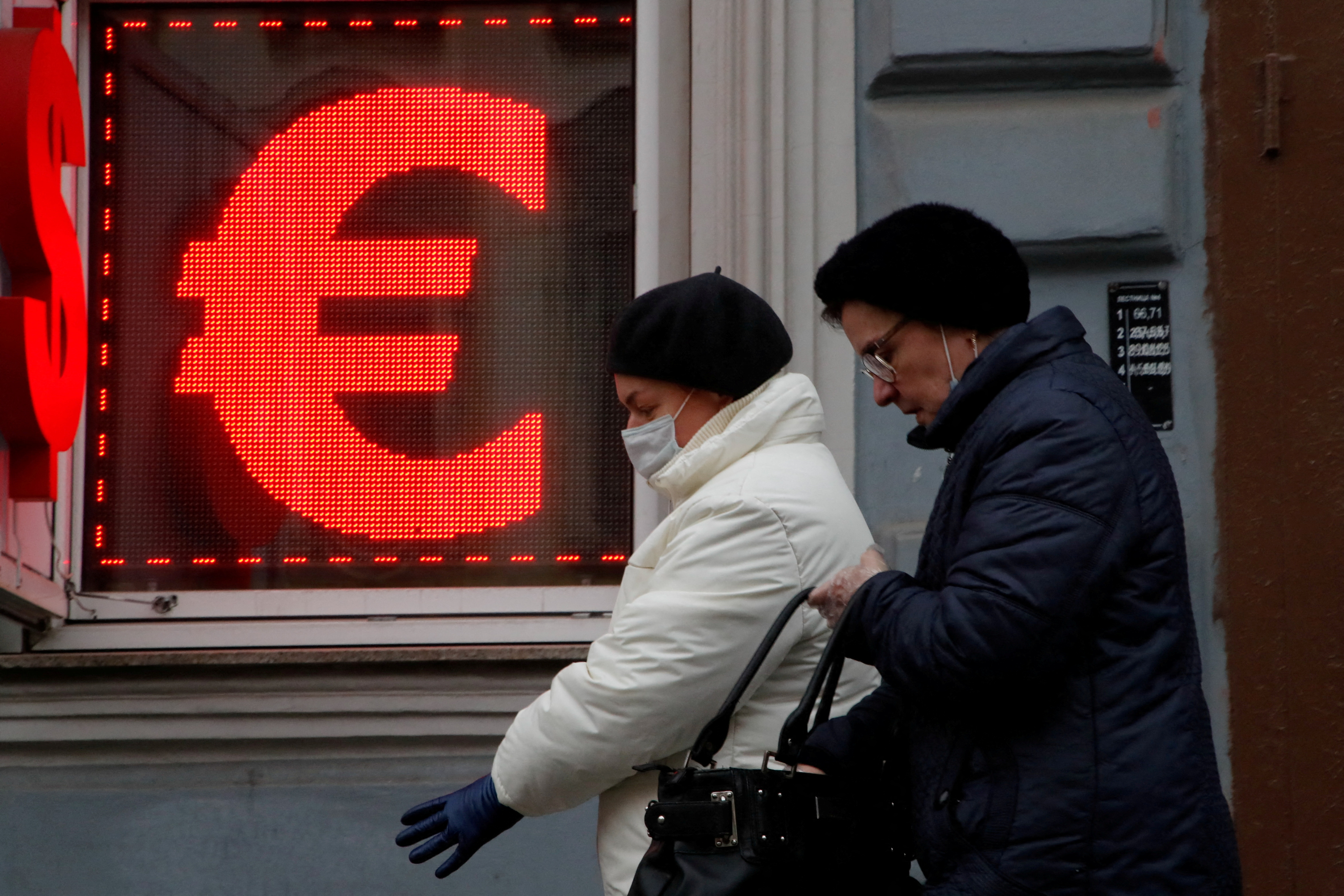 Women walk past a board showing the U.S. dollar and euro signs in Saint Petersburg