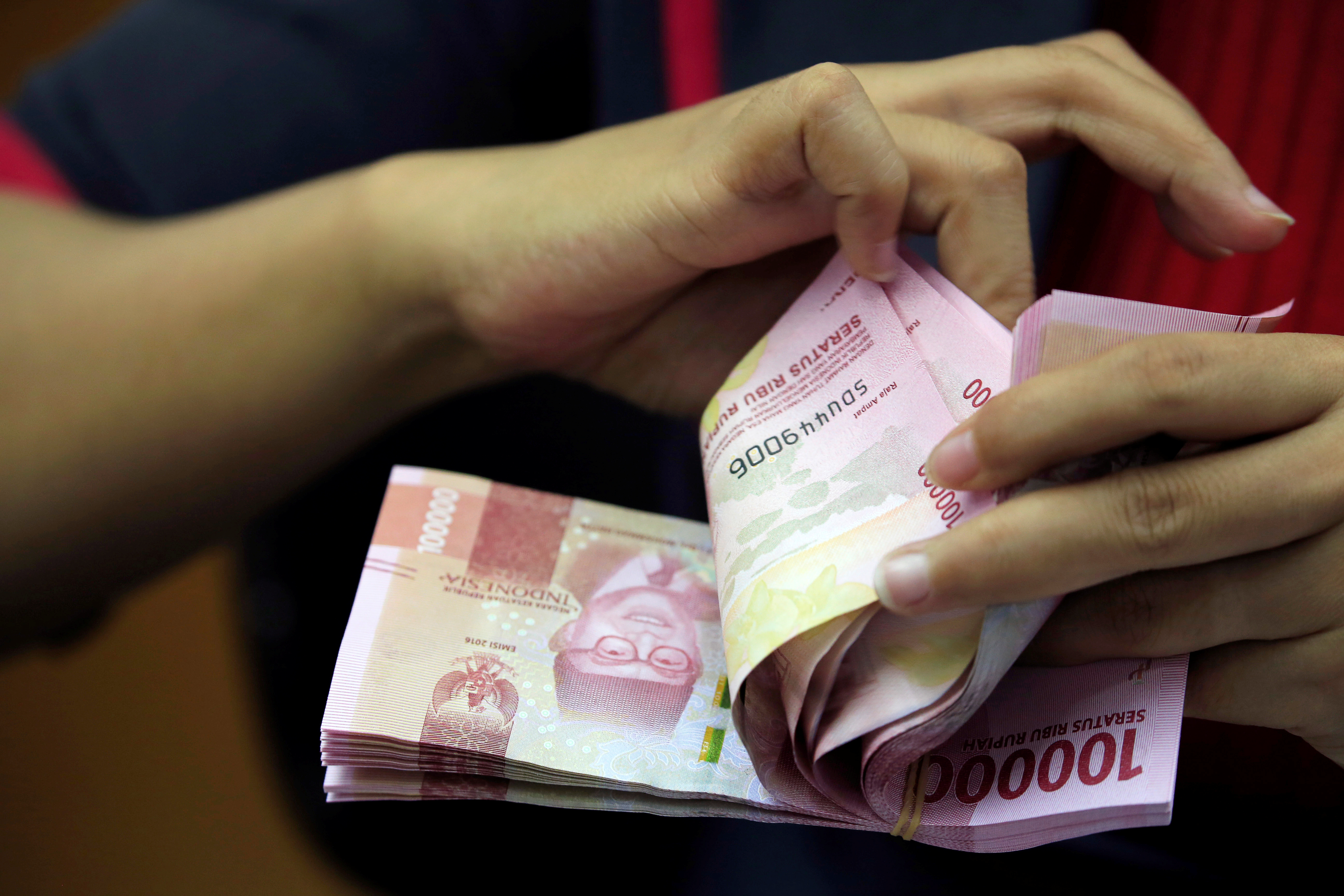 An employee counts Indonesian rupiah banknotes at a currency exchange office in Jakarta