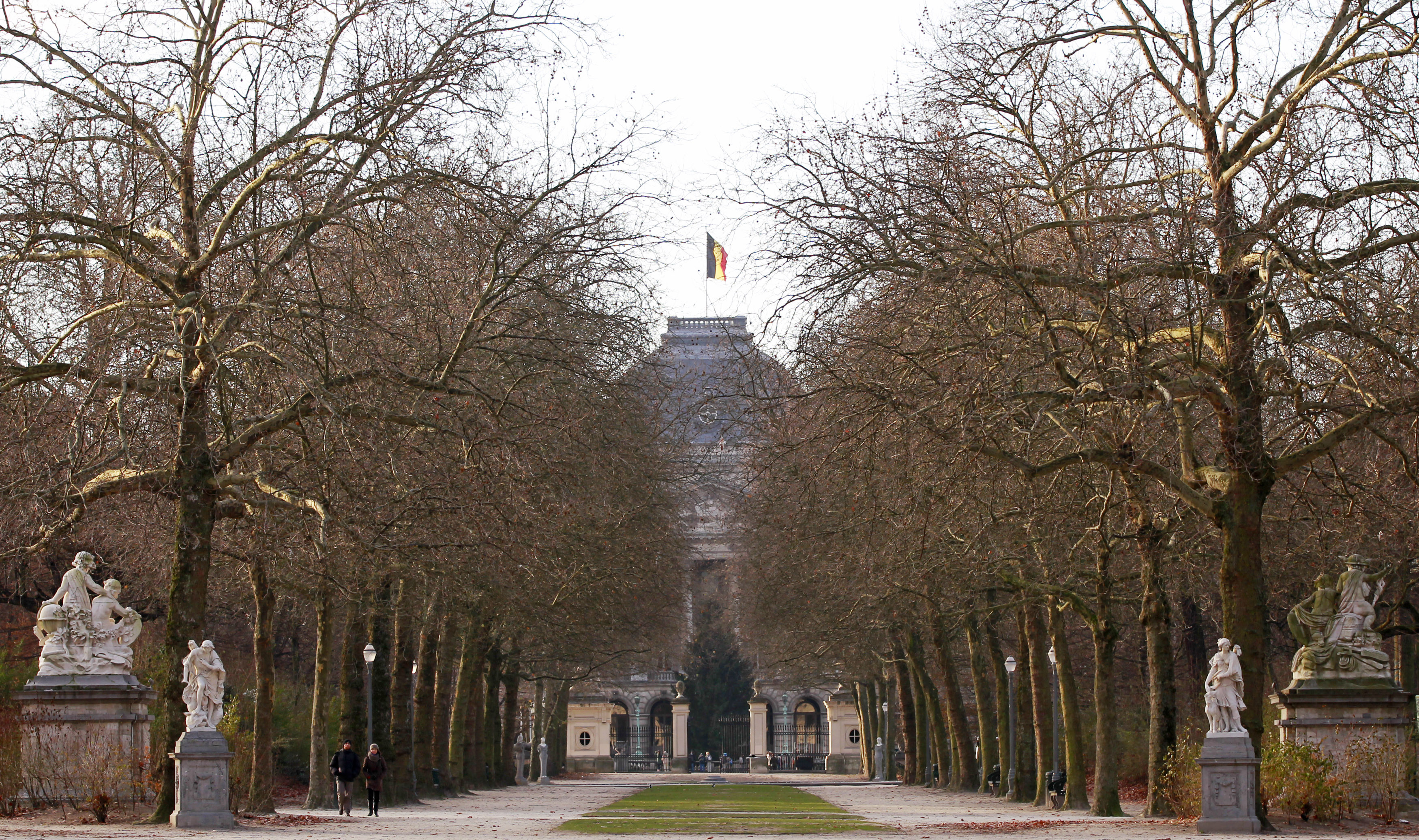 Pedestrians walk in a park as the Belgian national flag flies over the Royal Palace in Brussels