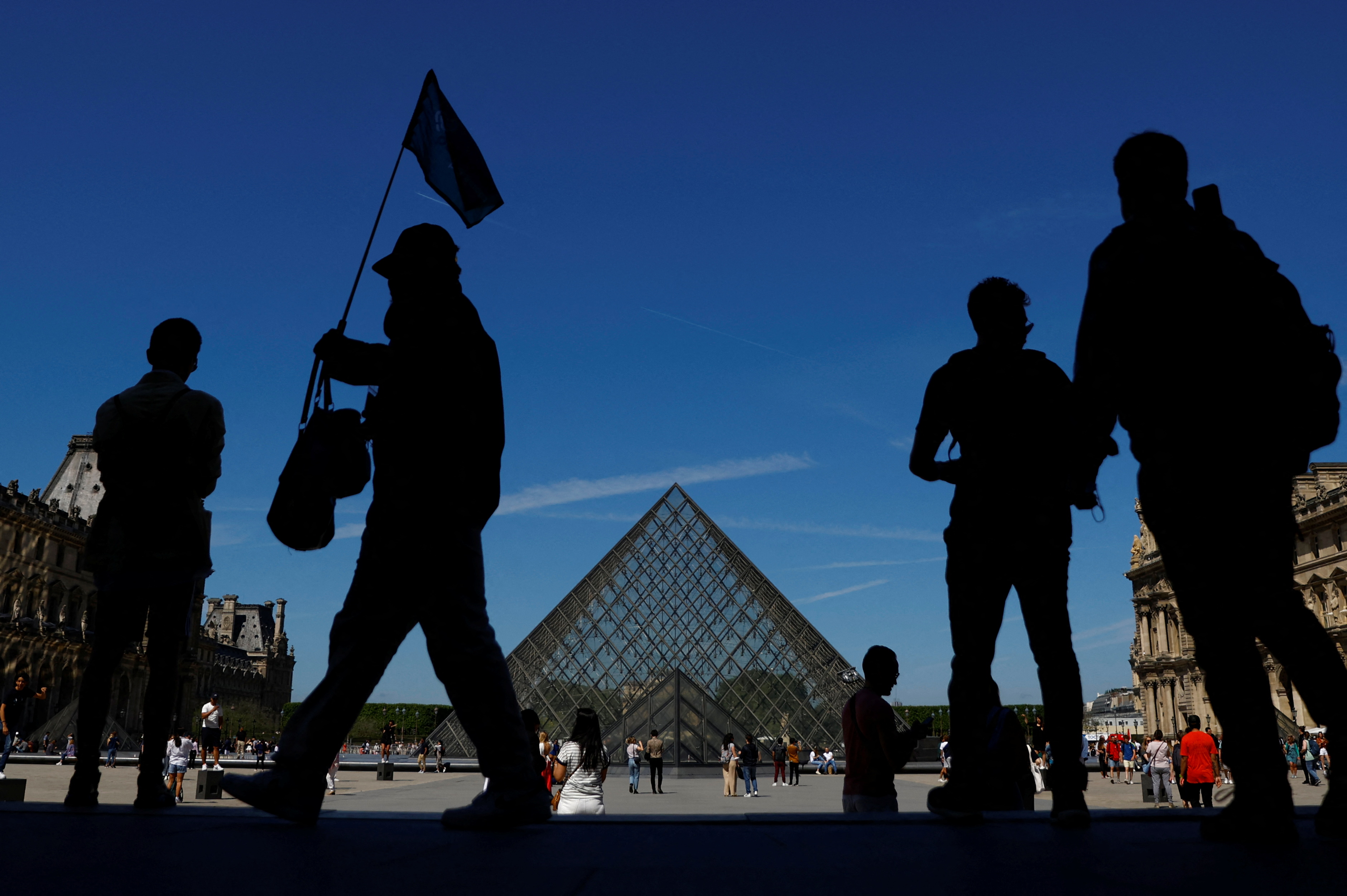 Tourists walk near the glass Pyramid of the Louvre museum in Paris