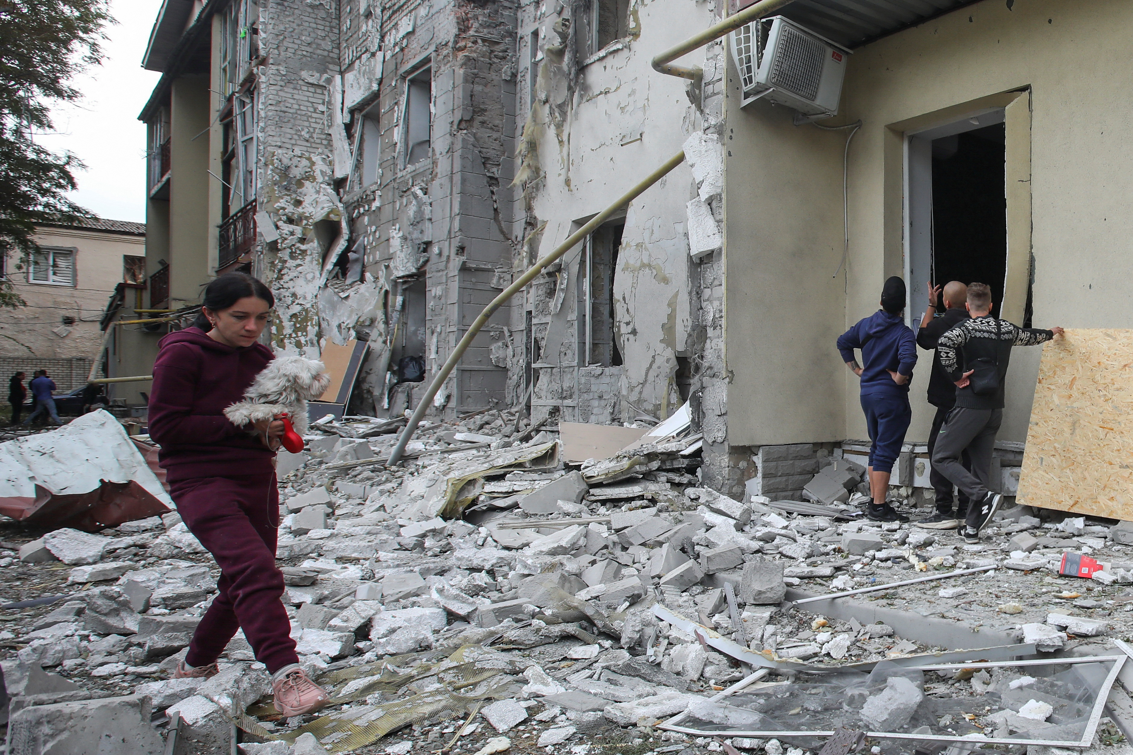Woman carries a dog in a front of a residential building damaged by a Russian missile strike in Kharkiv