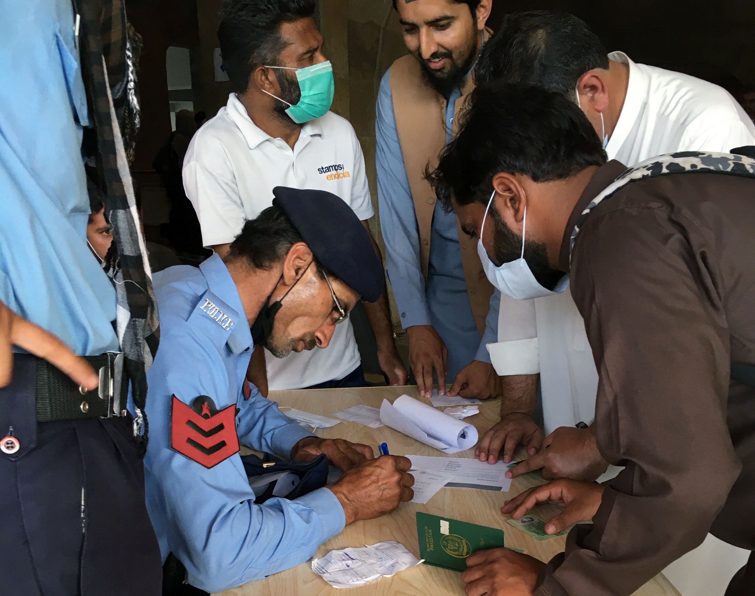 A police officer helps men to fill out forms to obtain a coronavirus disease (COVID-19) vaccine, so they can travel to work abroad, at a mass vaccination centre in Islamabad