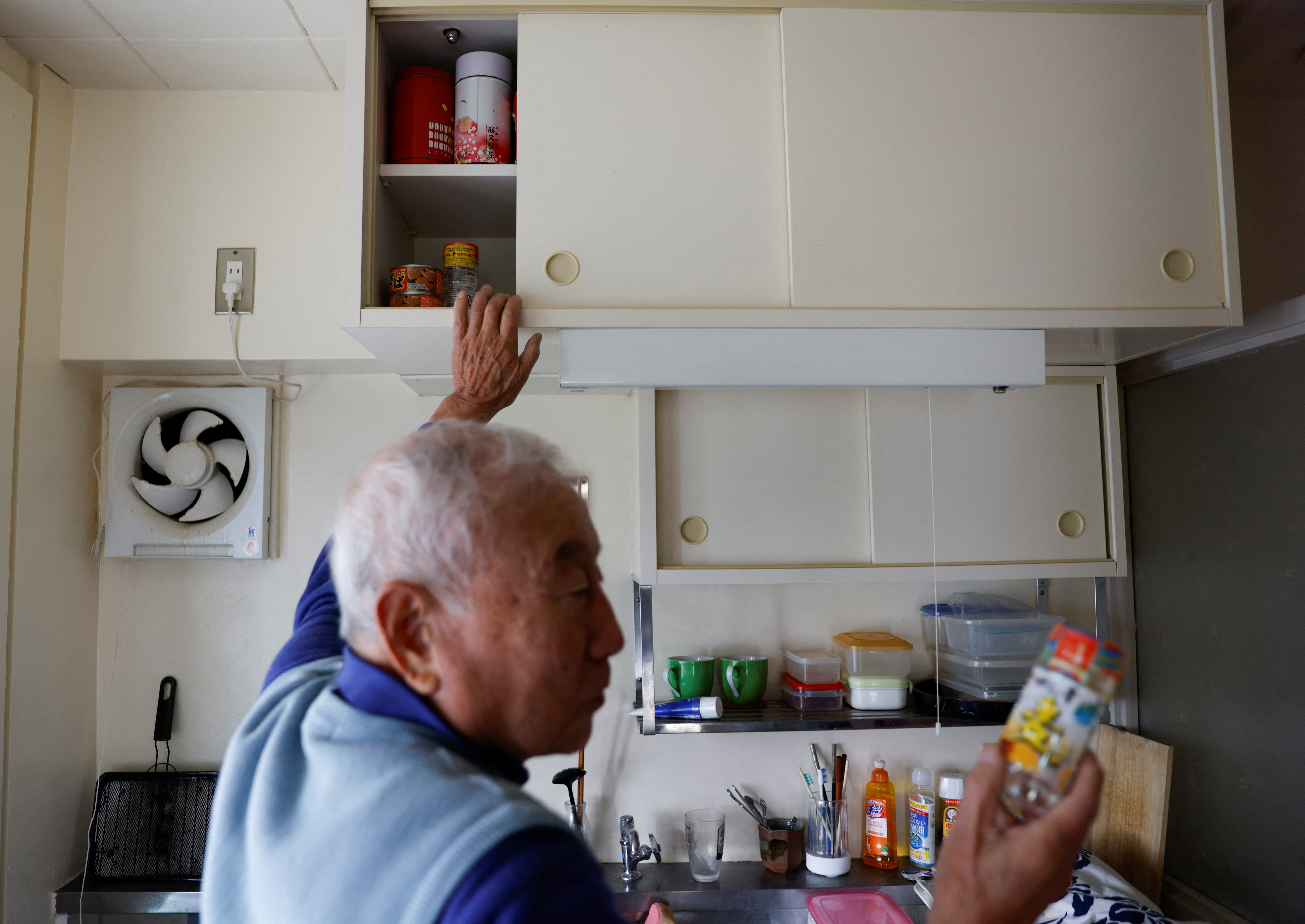 Pensioner Yoshio Koitabashi shows the contents of his small kitchen cabinet at his apartment in a public housing complex in Tokyo