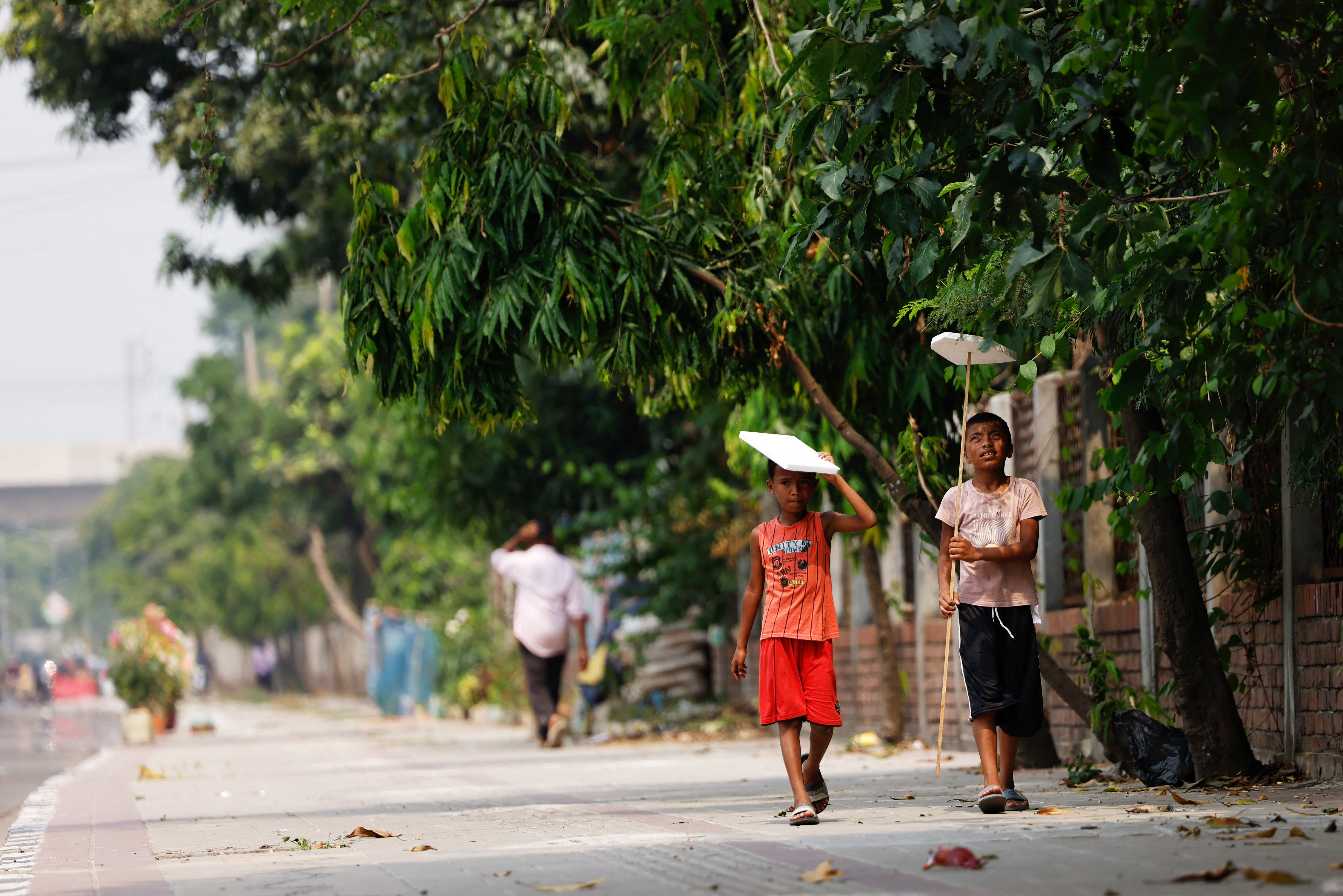 Children hold cork sheets to cover them from the sun while walking along a street during a countrywide heatwave in Dhaka