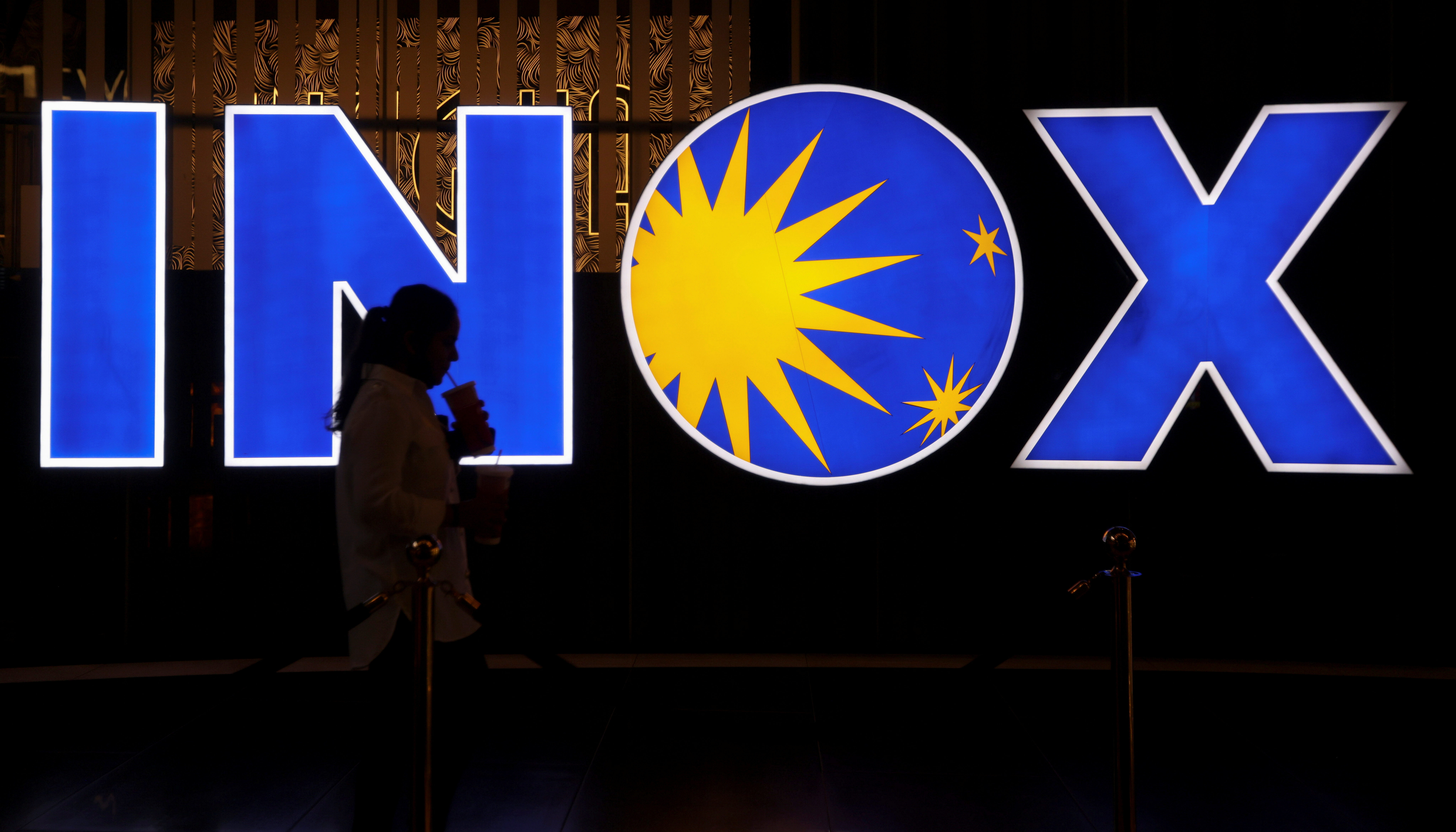 A woman walks past a logo of the INOX movie theatre at a cinema hall in Mumbai
