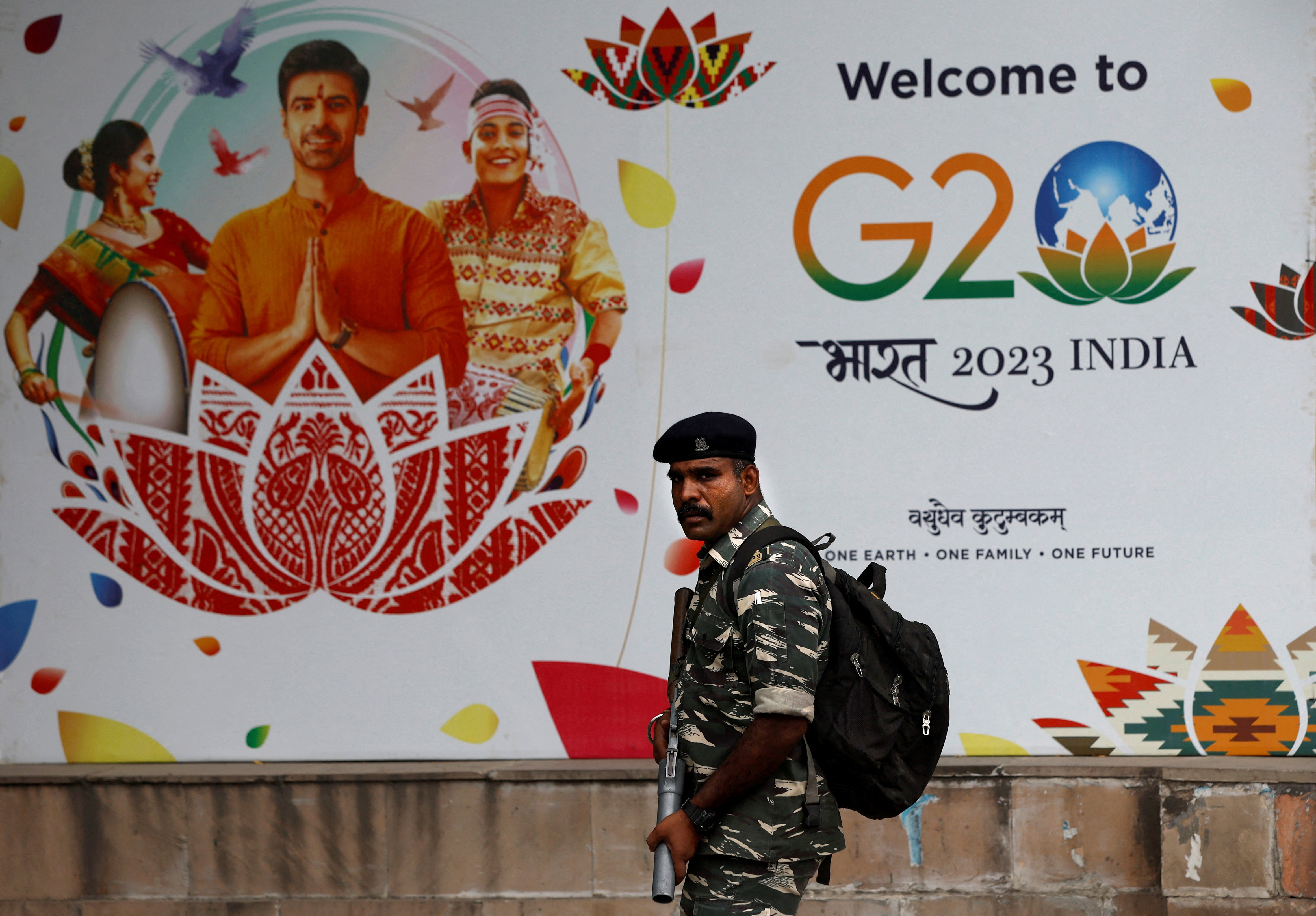 A Central Reserve Police Force personnel patrols a road next to a hoarding ahead of the G20 Summit in New Delhi