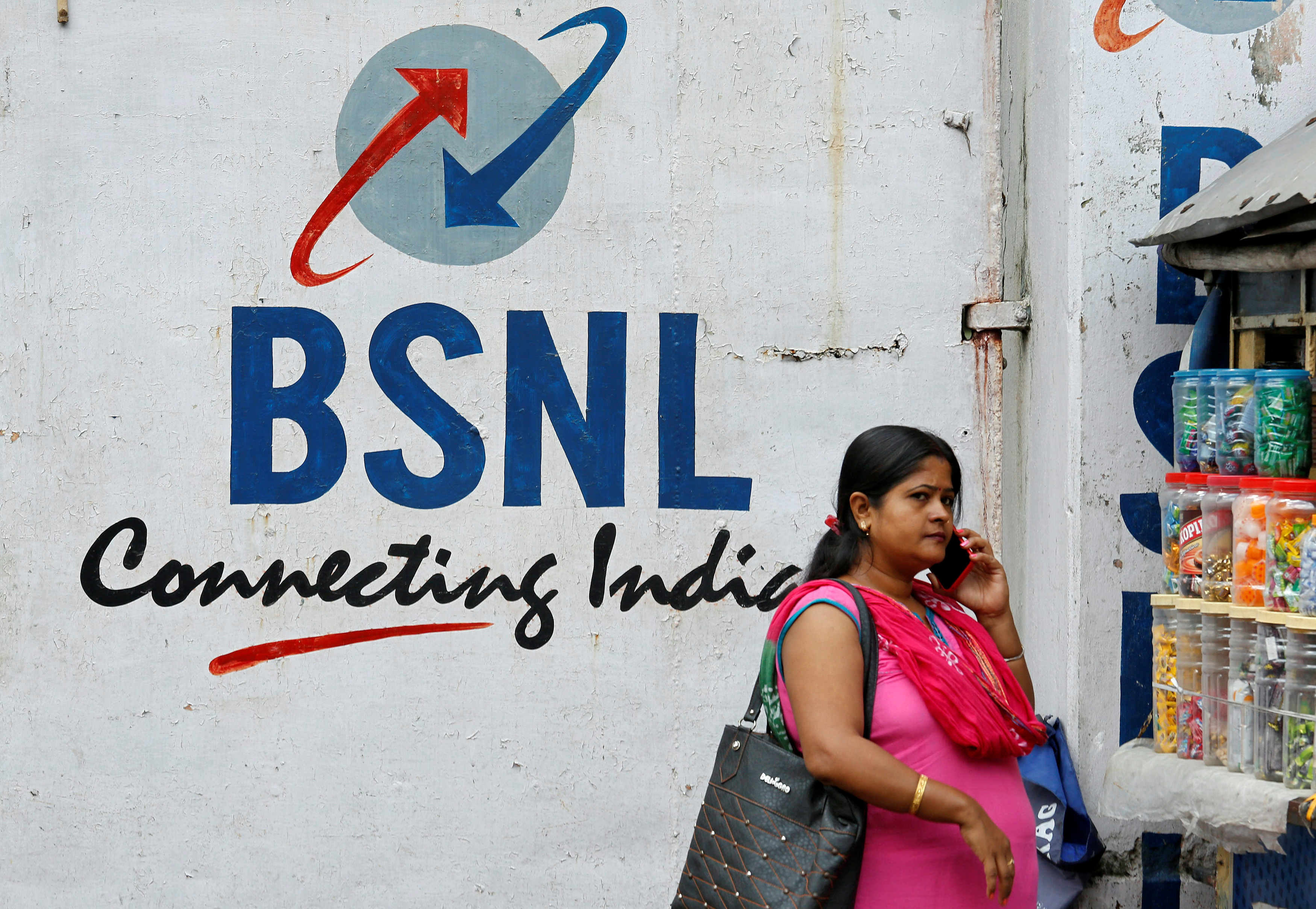 A woman speaks on her mobile phone in front of the logo of Bharat Sanchar Nigam Ltd (BSNL) painted on a wall outside its office in Kolkata