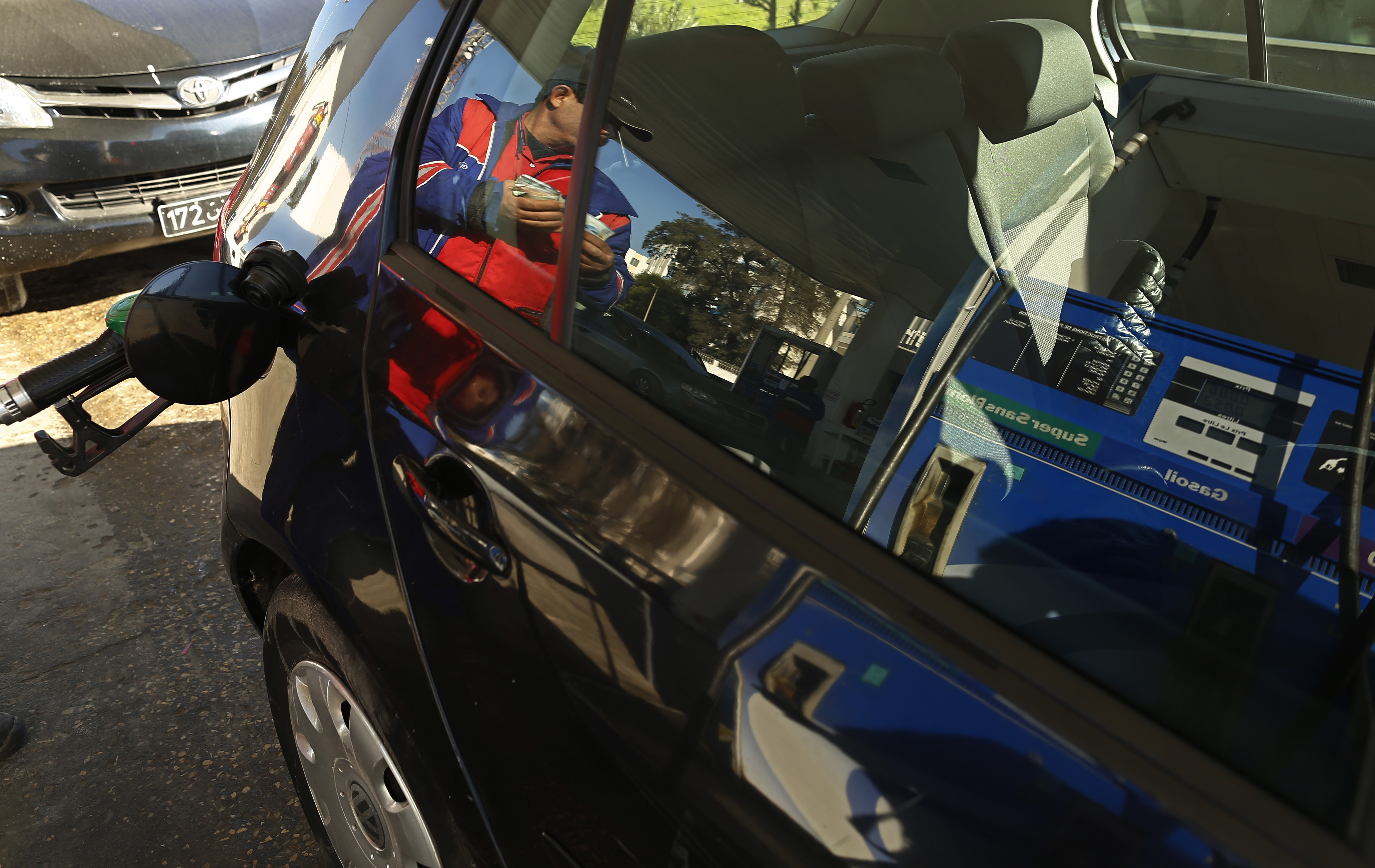 A worker stands beside a fuel pump as he is reflected  on a car window at Agil gas station in Tunis
