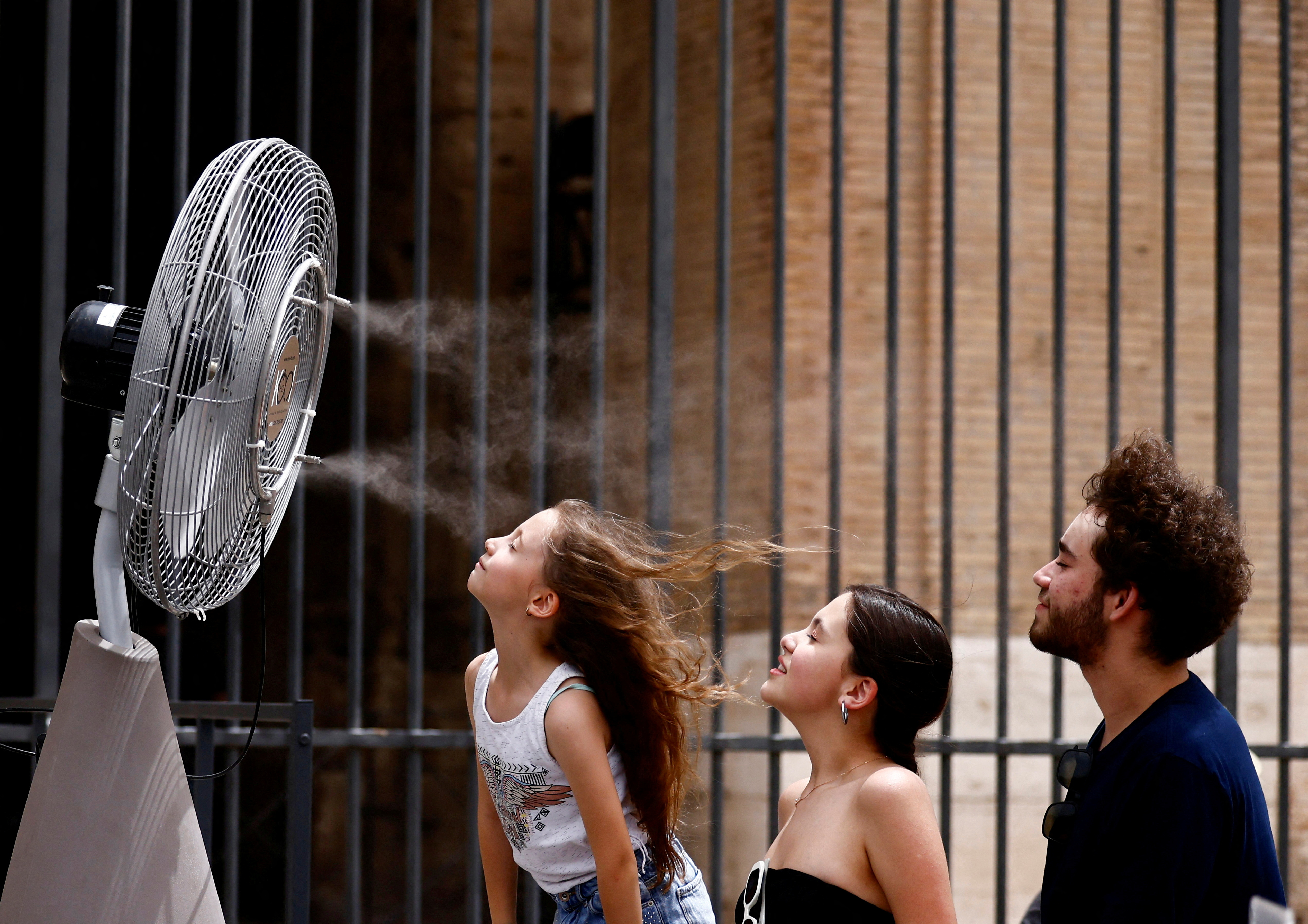 People stand in front of a cooler installed around the Colosseum amid a heatwave in Rome