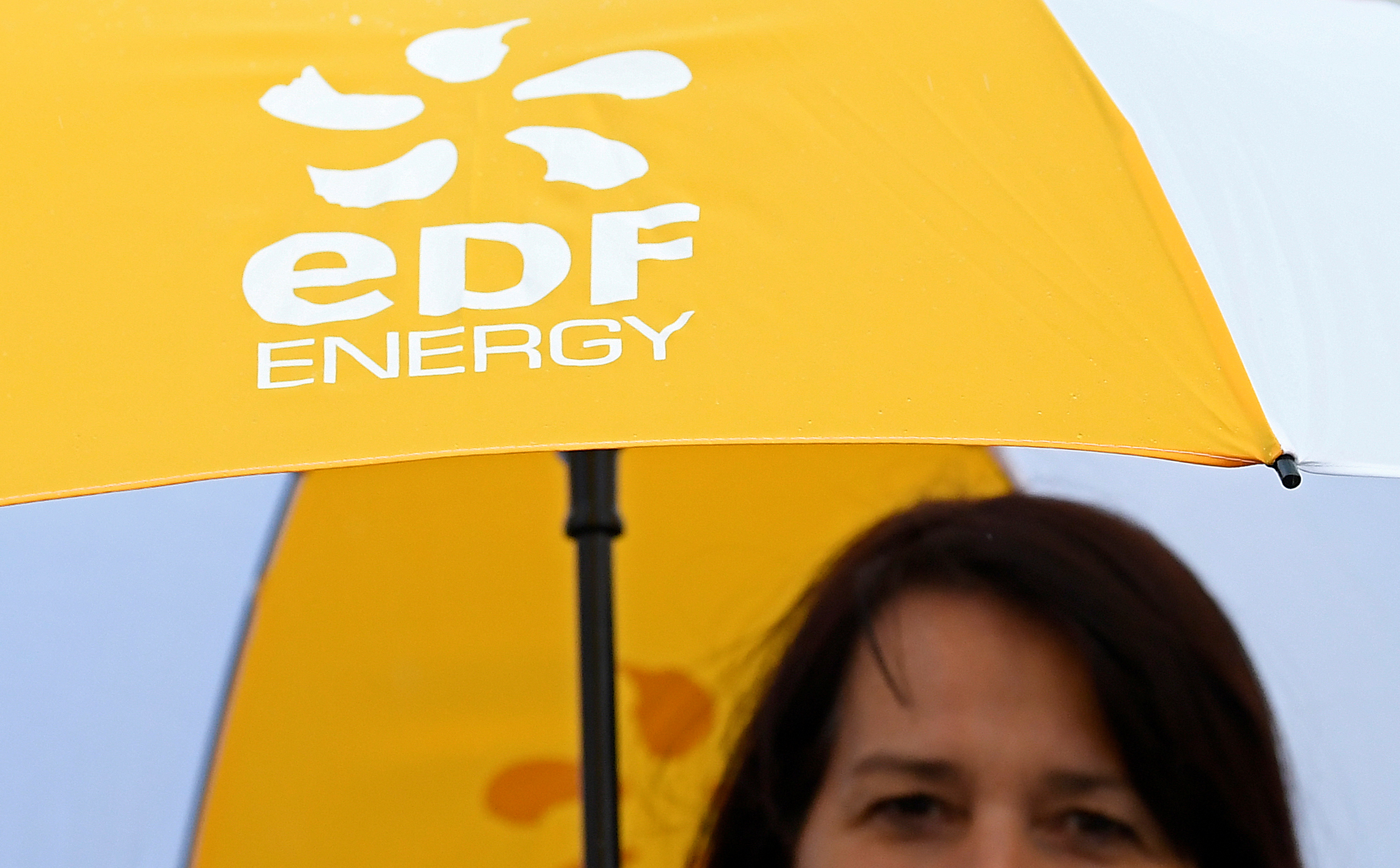 An employee carries an umbrella with the EDF energy logo near the Hinkley Point C nuclear power station near Cannington in southwest England