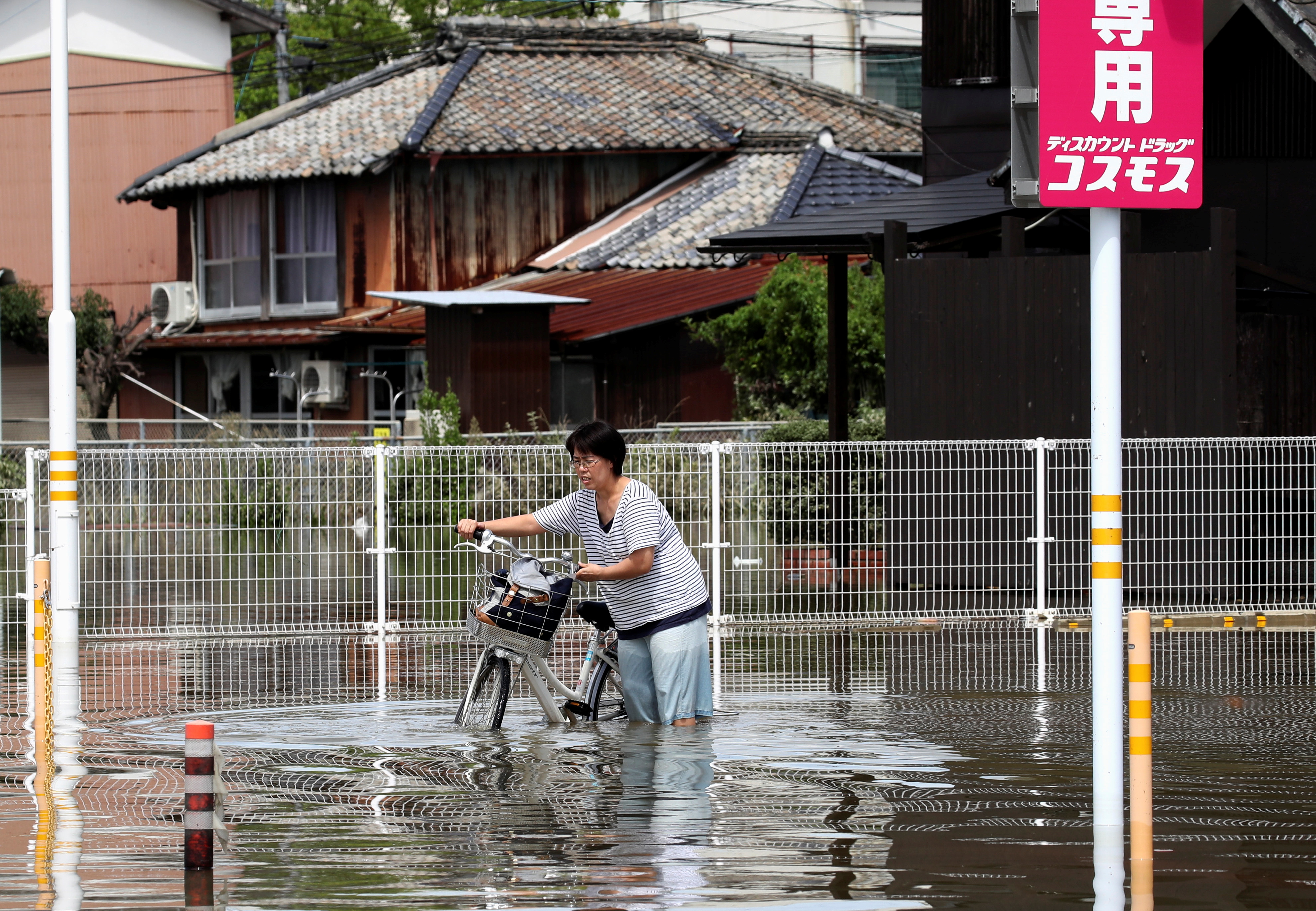 A woman pushes a bicycle through a flooded street in Takeo, Saga Prefecture, western Japan