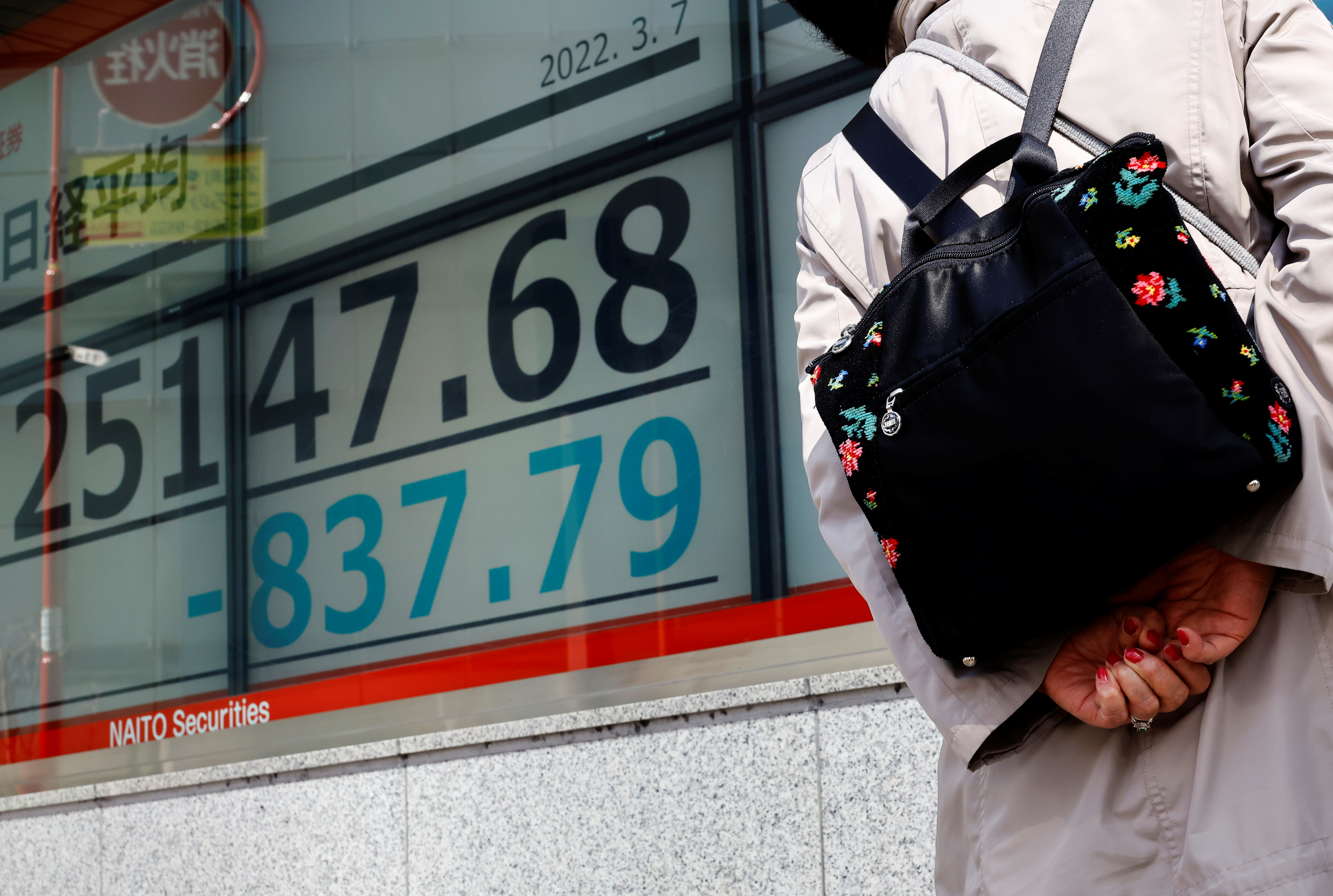 A woman wearing a protective mask, amid the coronavirus disease (COVID-19) outbreak, looks at an electronic board displaying Japan's Nikkei index outside a brokerage in Tokyo