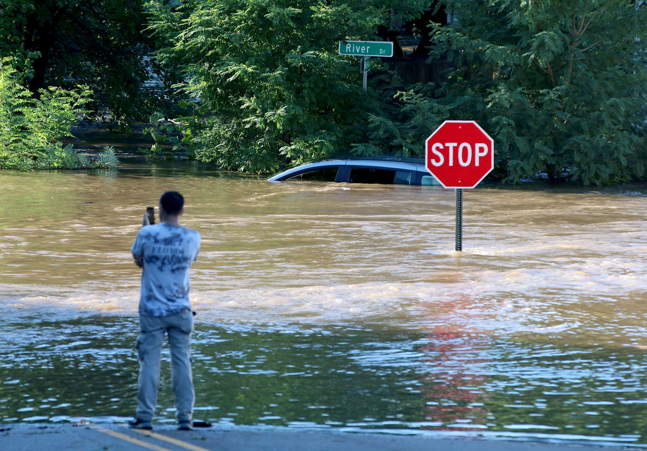 A man takes photos of a submerged car in Passaic