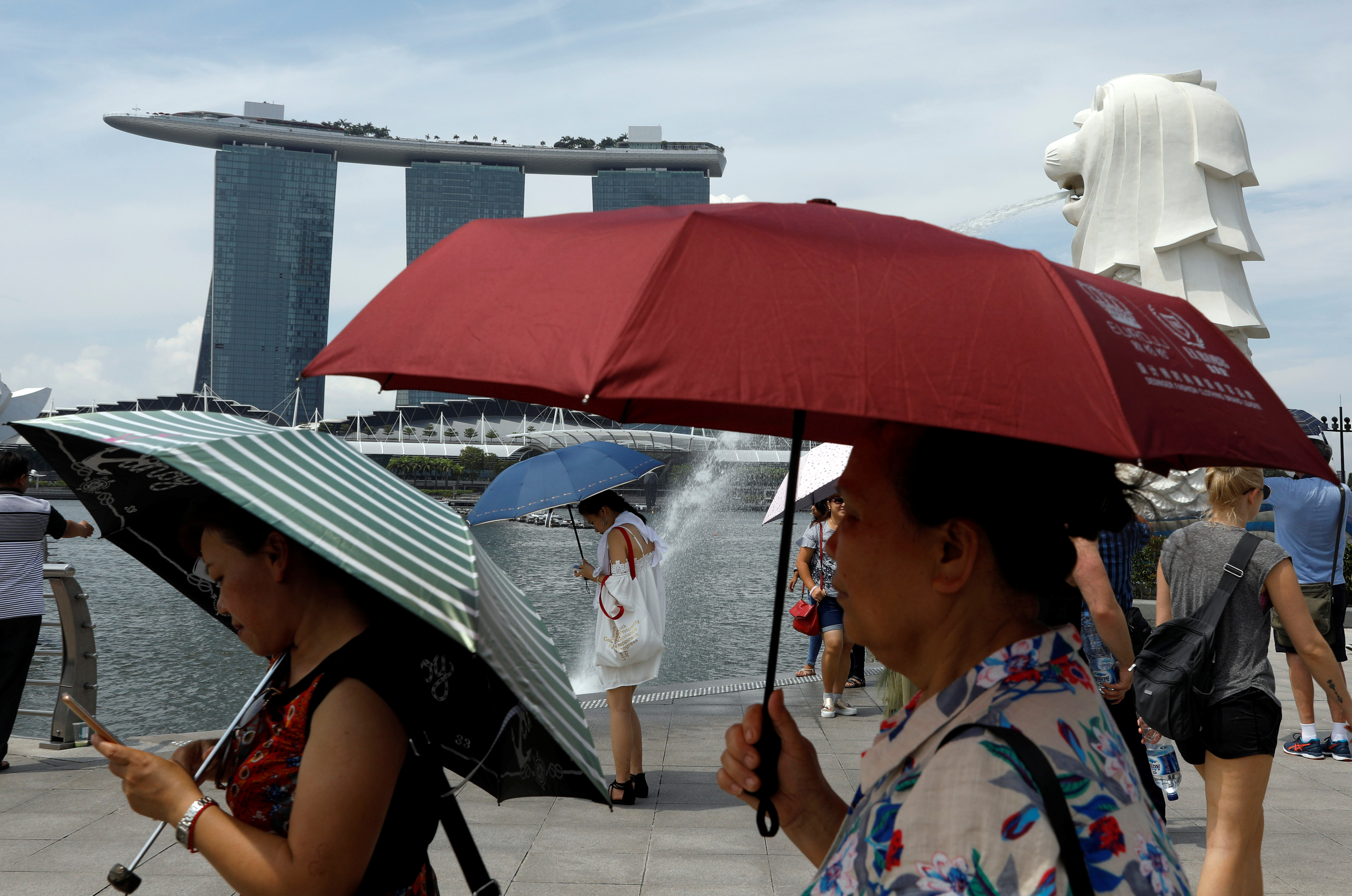 Tourists shield themselves with umbrellas on a hot day at the Merlion Park in Singapore