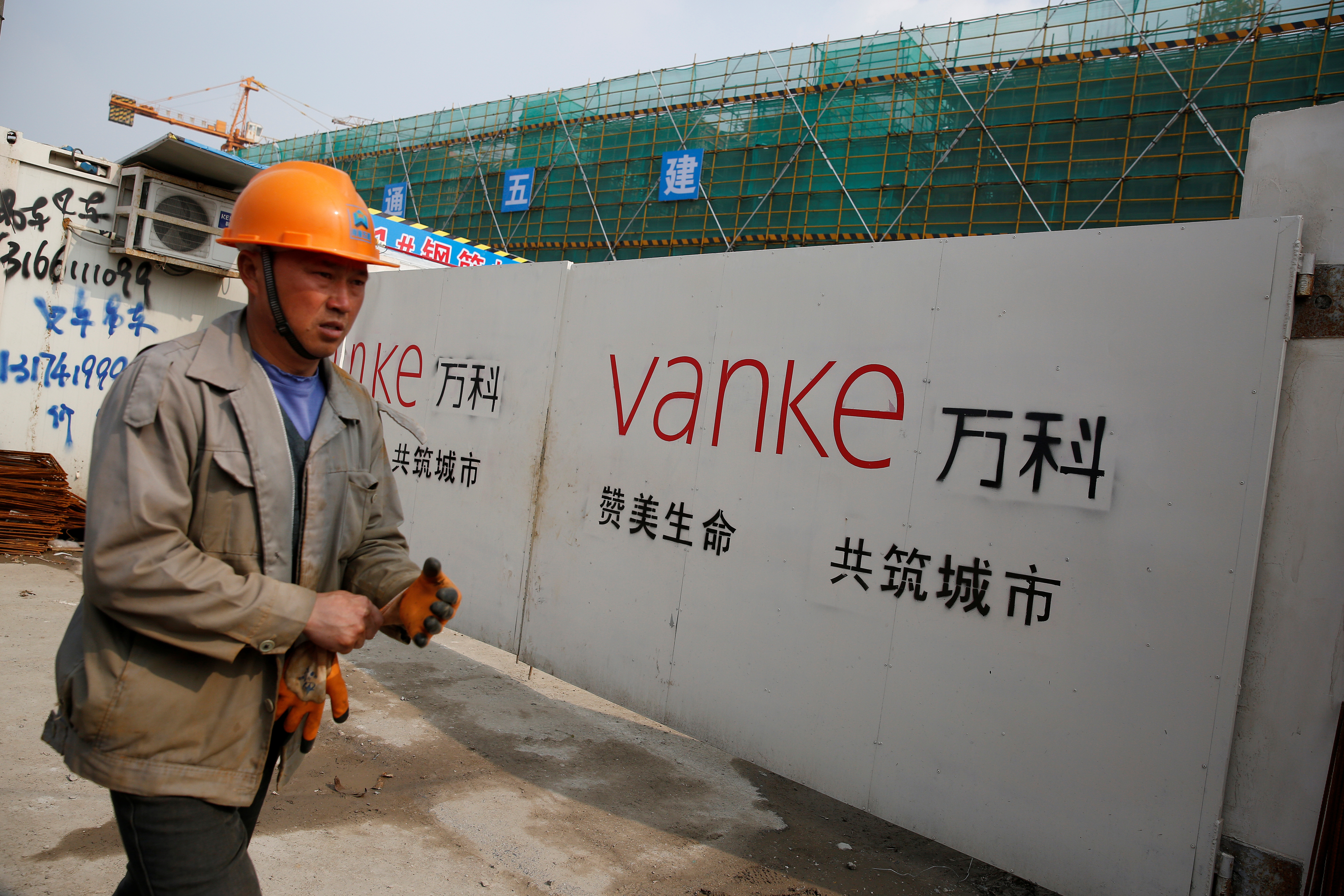 A person walks past by a gate with a sign of Vanke at a construction site in Shanghai