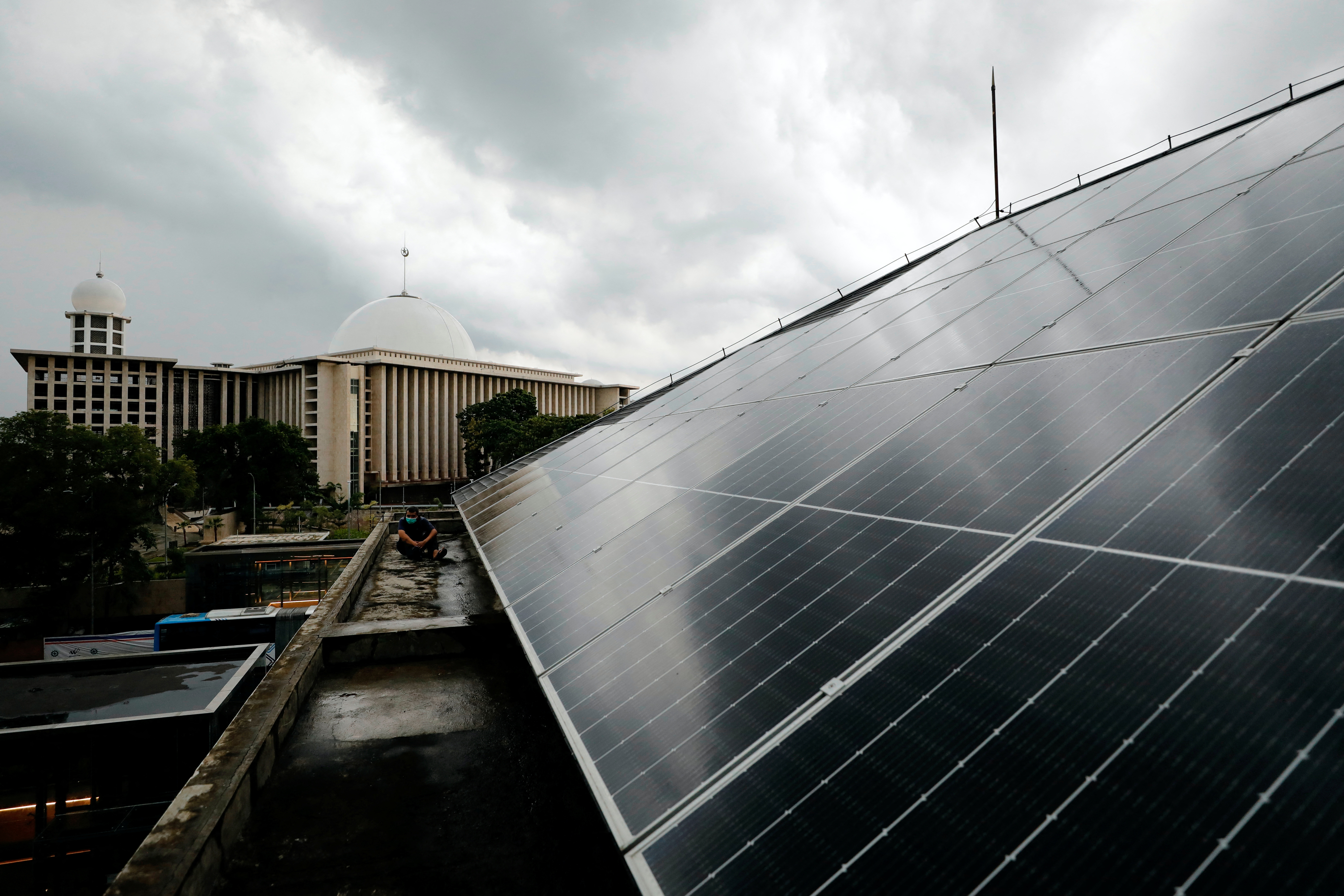A technician sits on the roof of a building that is installed with solar panels, at the Jakarta Catedral in Jakarta