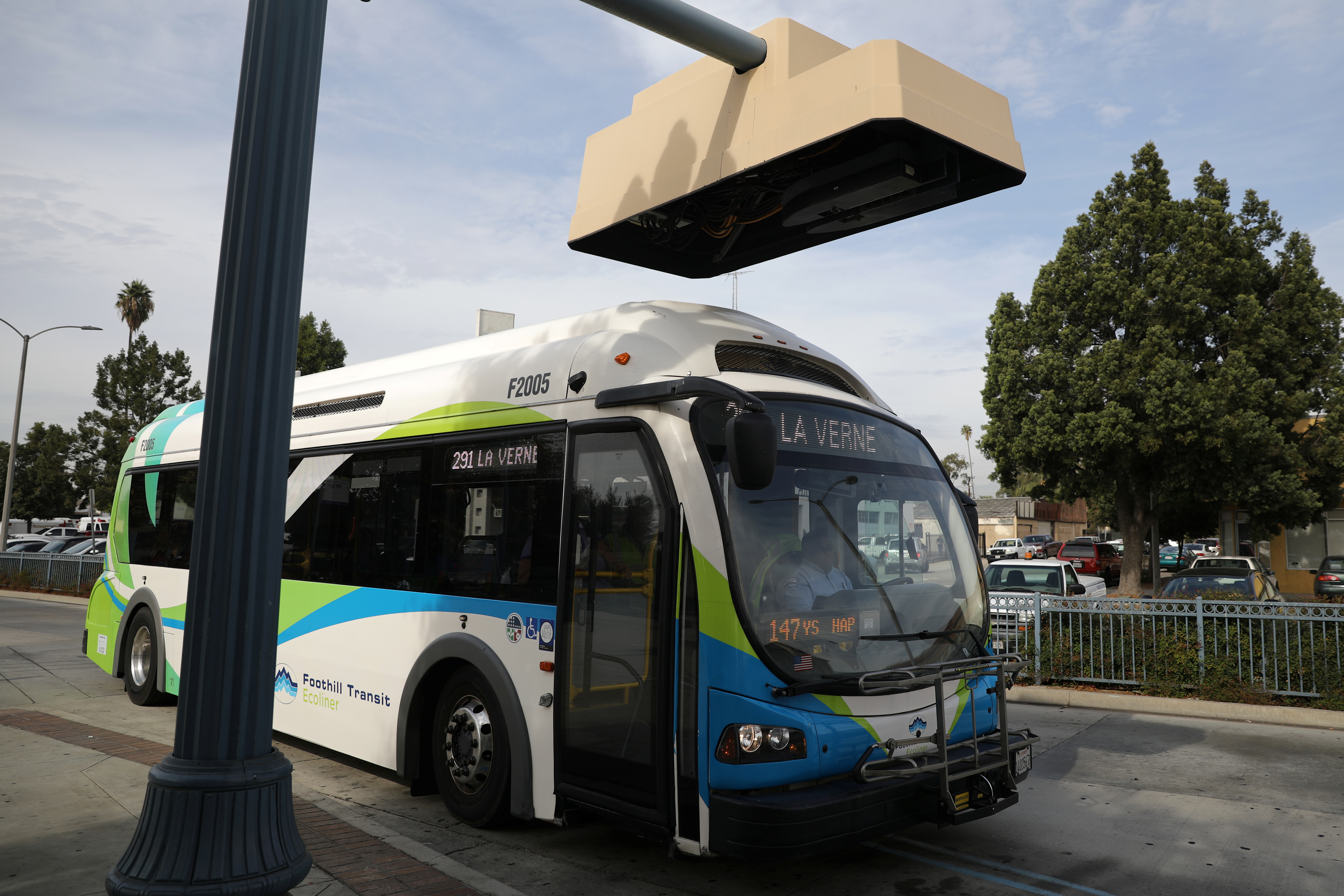 An electric bus sits under a charging station in Pomona