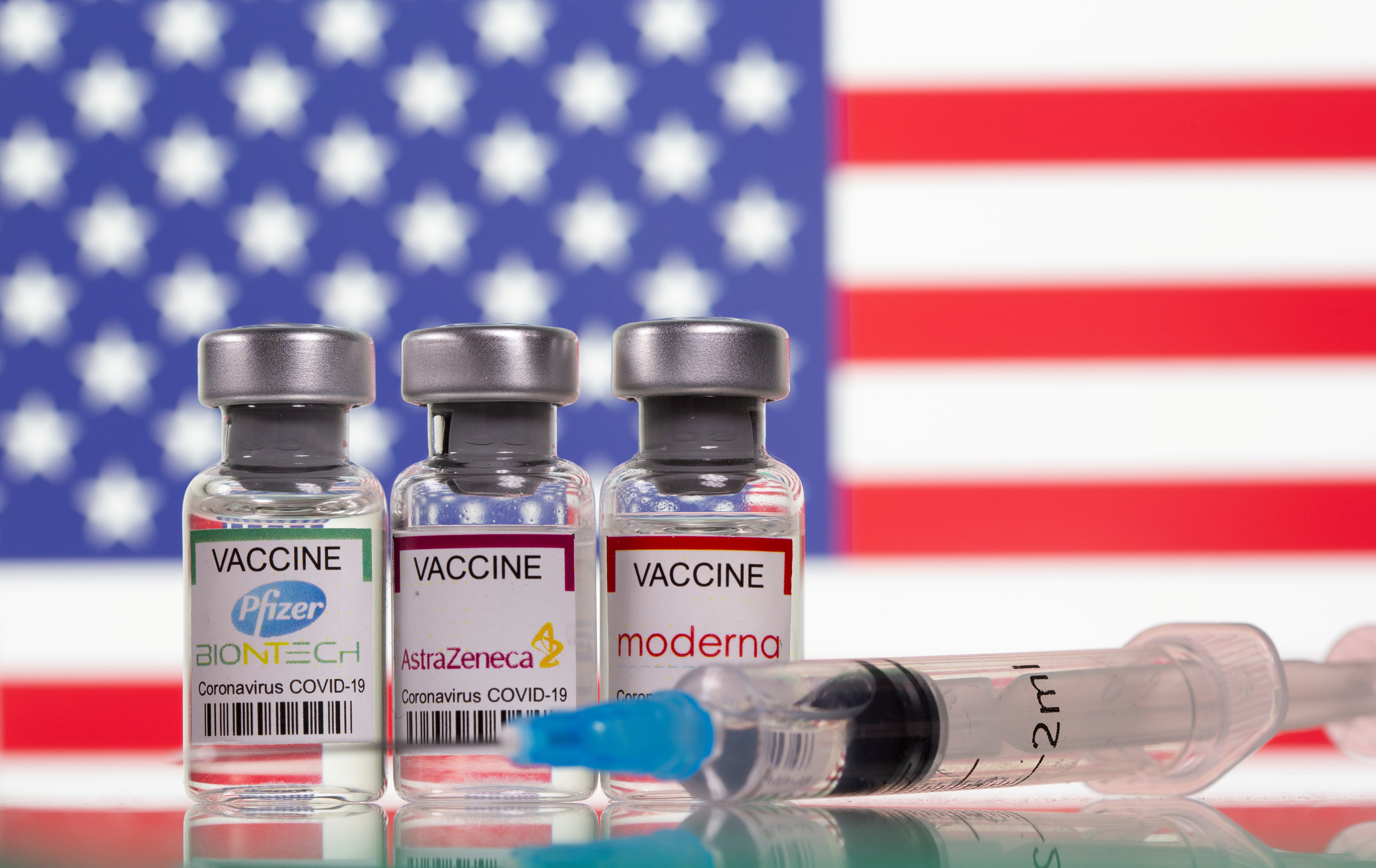 Vials with Pfizer-BioNTech, AstraZeneca, and Moderna coronavirus disease (COVID-19) vaccine labels are seen in front of a U.S. flag in this illustration picture taken March 19, 2021. REUTERS/Dado Ruvic/Illustration/File Photo