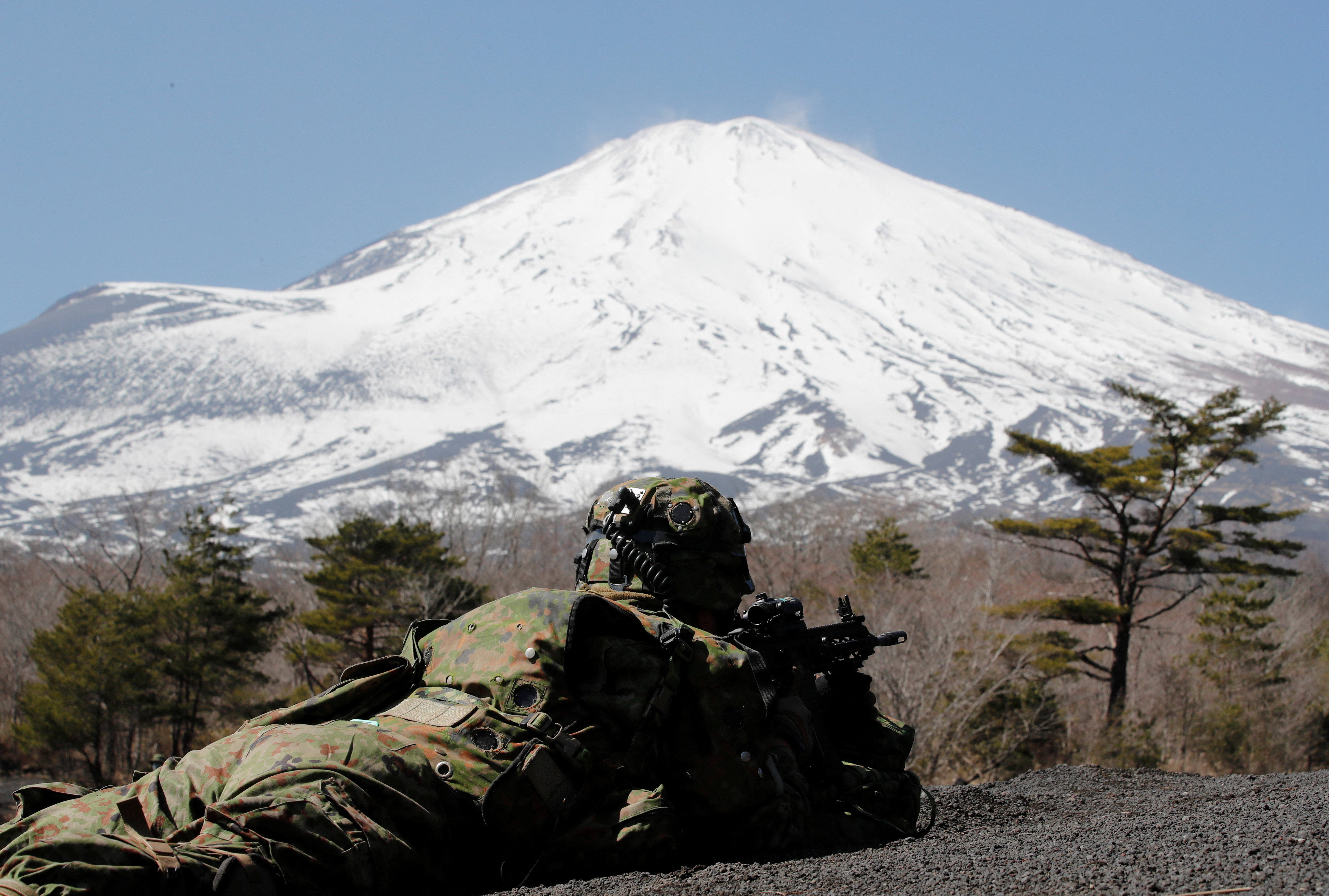 Mt.Fuji is seen while a member of the Japanese Self-Defense Force’s Amphibious Rapid Deployment Brigade takes a position during joint airborne landing exercises with U.S. marines in Gotemba