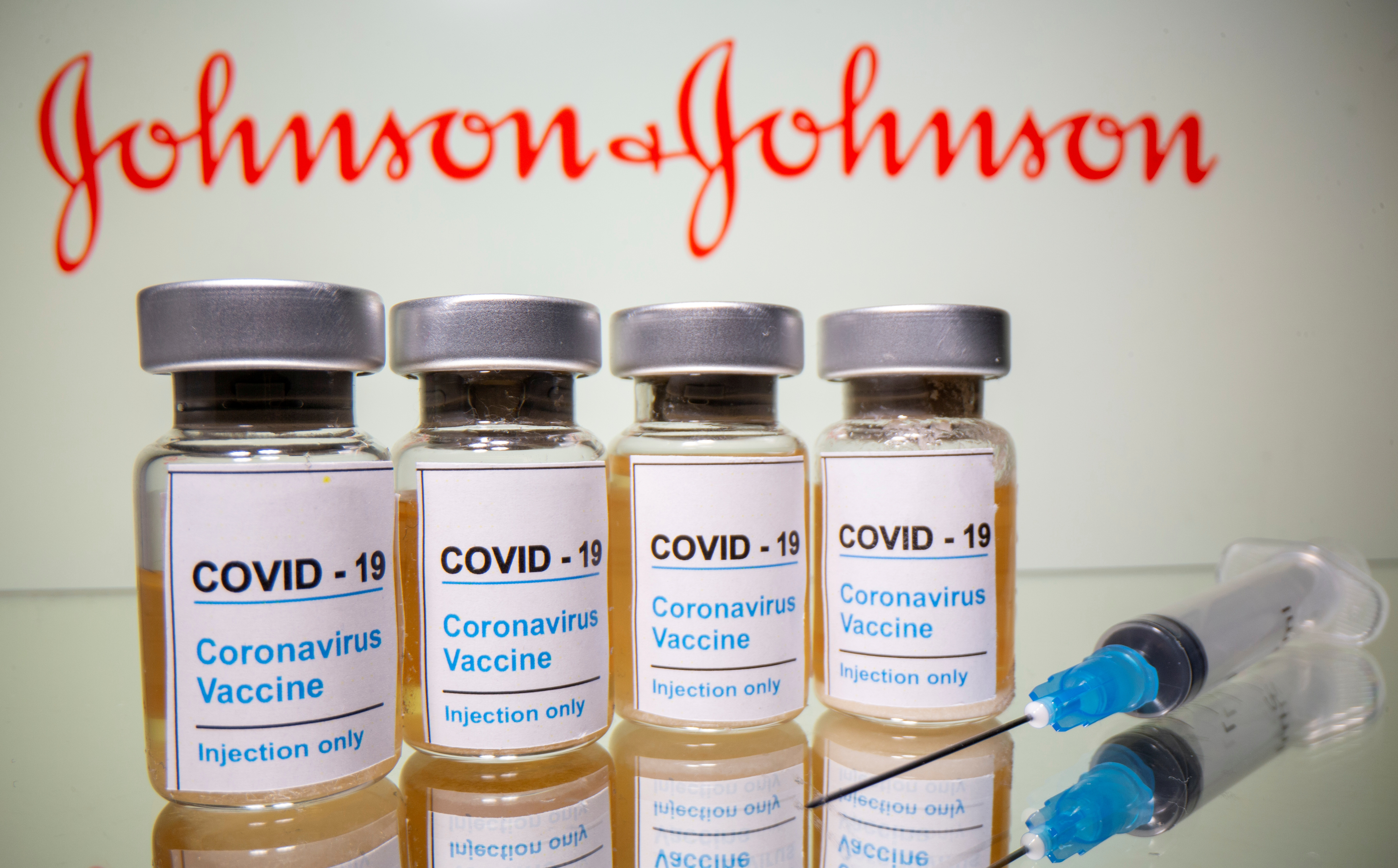 Vials and medical syringe are seen in front of J&J logo in this illustration
