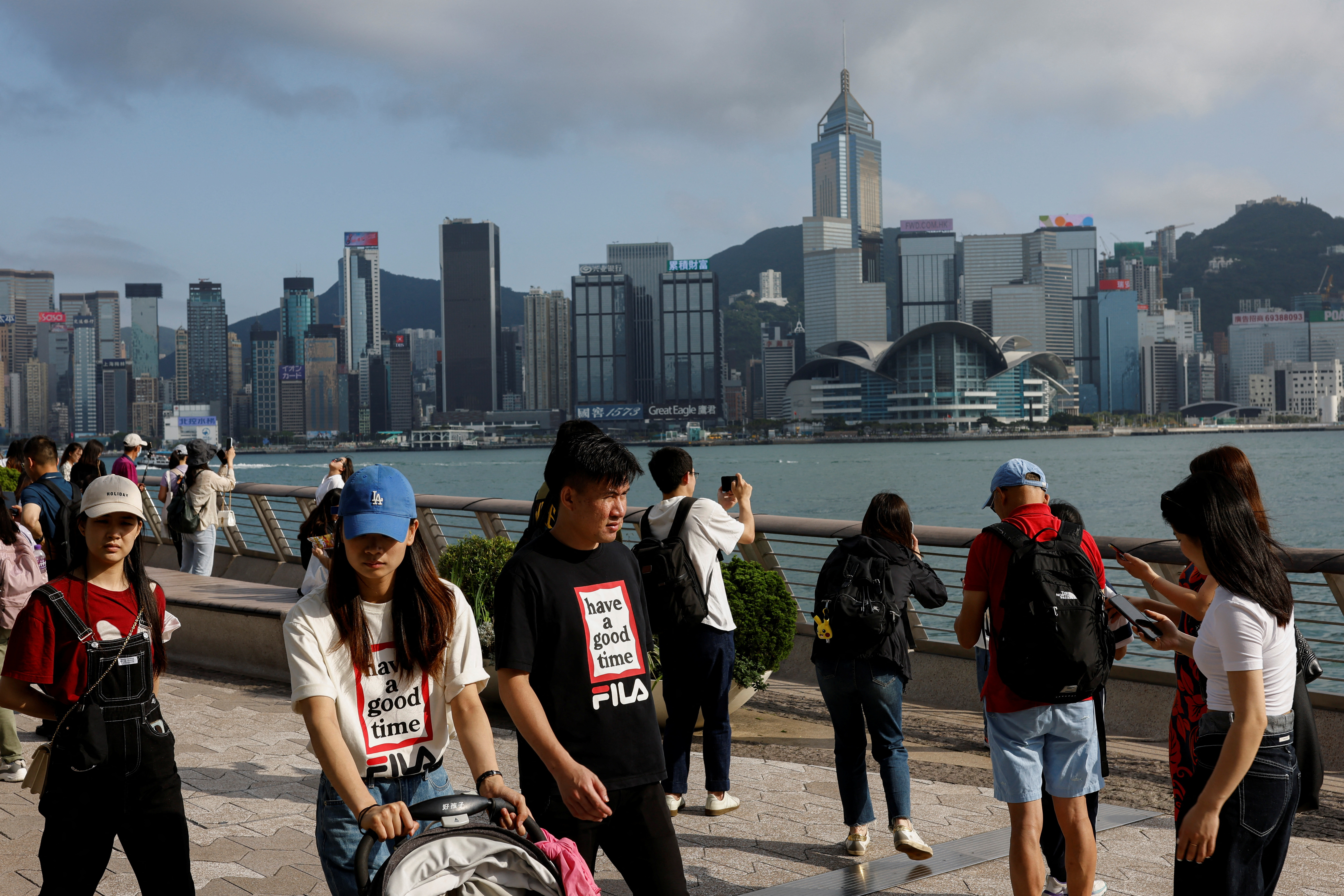 Mainland Chinese tourists walk in front of the skyline of buildings at Tsim Sha Tsui, in Hong Kong
