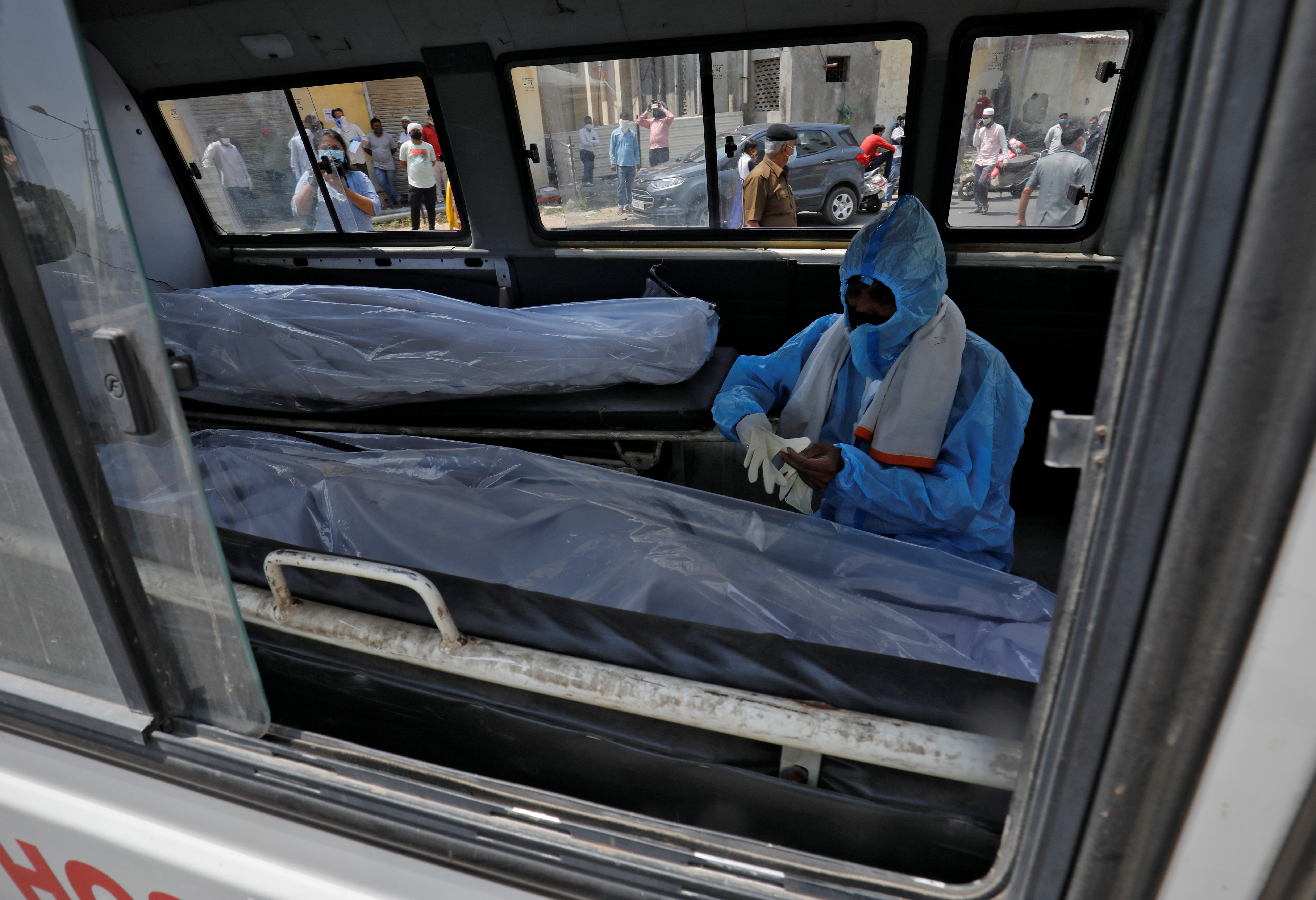A man wearing a protective suit sits next to the bodies of the victims of the coronavirus disease (COVID-19) inside an ambulance at a mortuary of a COVID-19 hospital in Ahmedabad