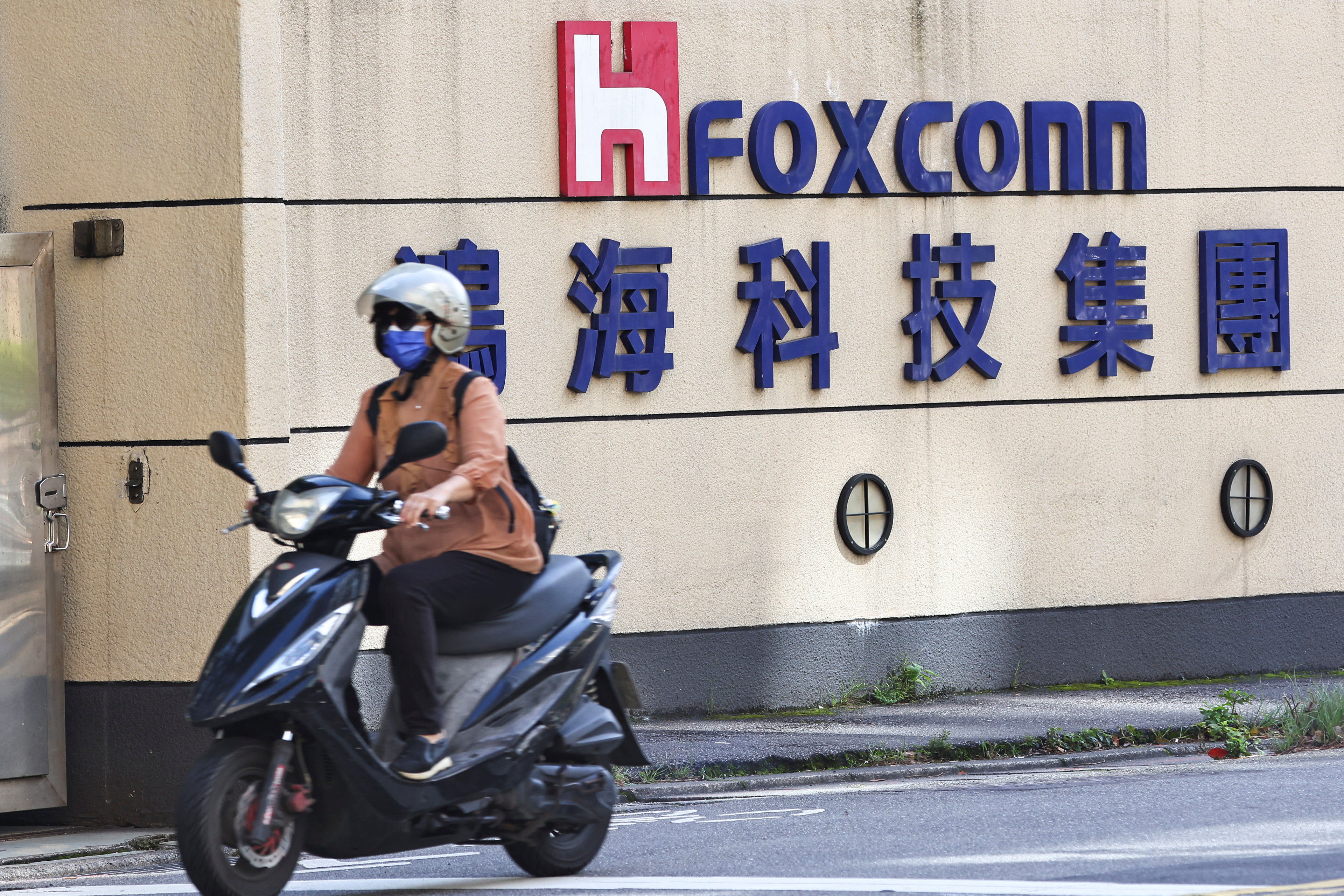 Kobieta przejeżdża obok logo Foxconn przed budynkiem firmy w Tajpej